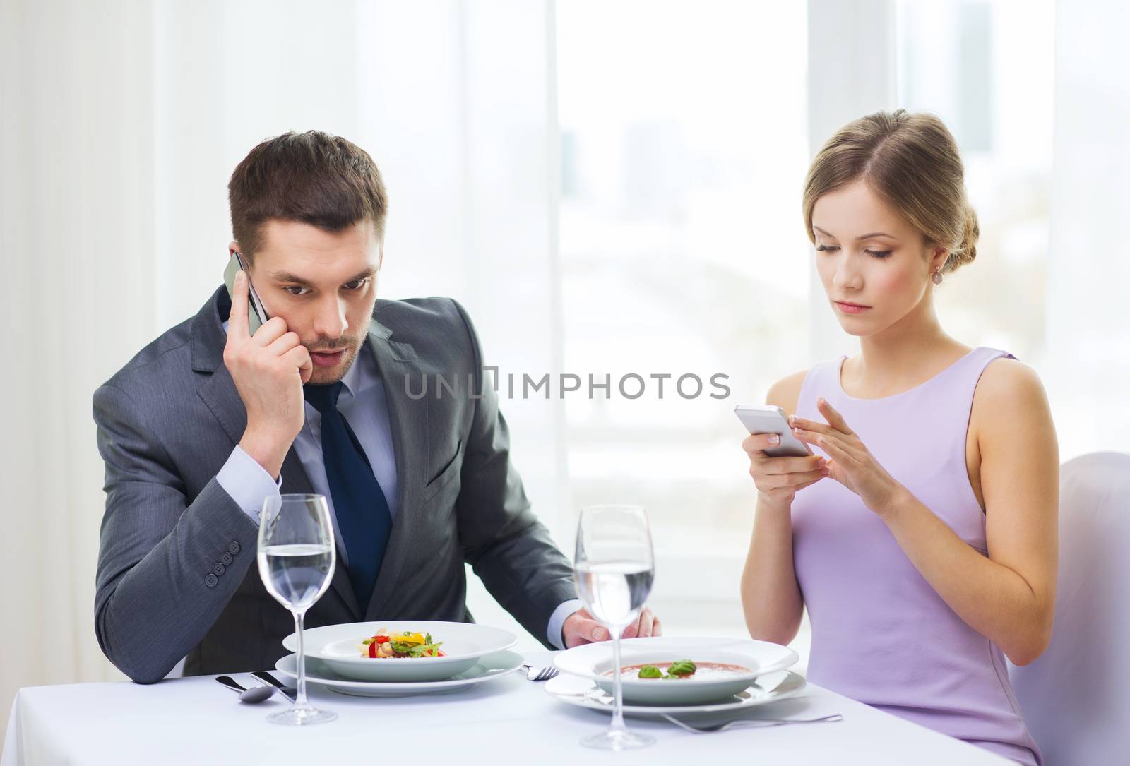 restaurant, couple, technology and holiday concept - busy couple with smartphones at restaurant