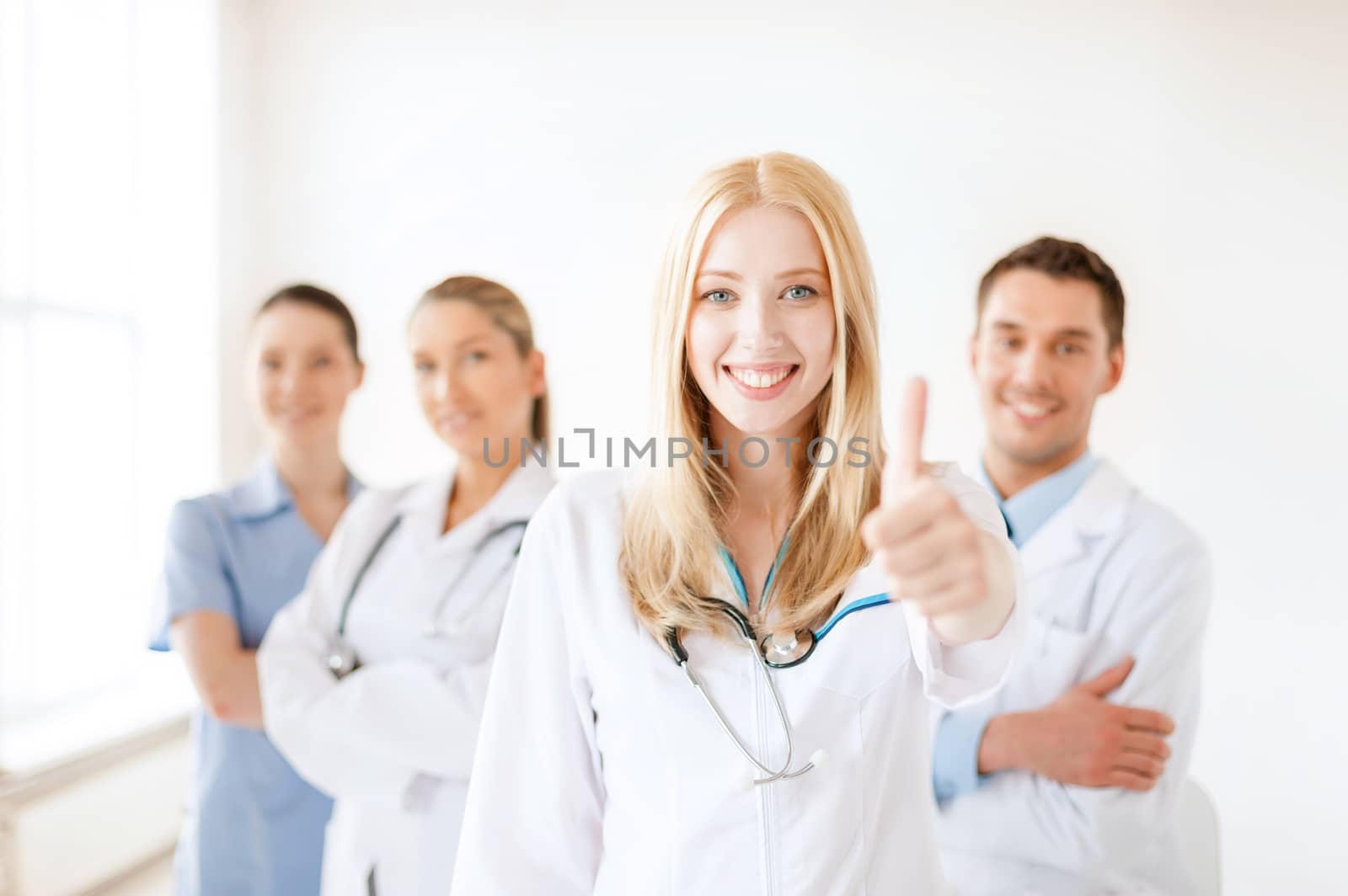 healthcare and medicine concept - attractive female doctor or nurse in front of medical group in hospital showint thumbs up