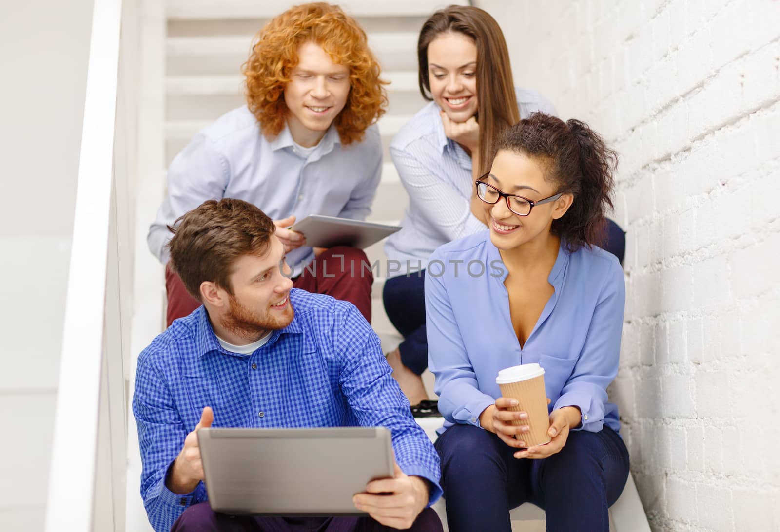 business, technology and startup concept - smiling creative team with laptop and tablet pc computer sitting on staircase