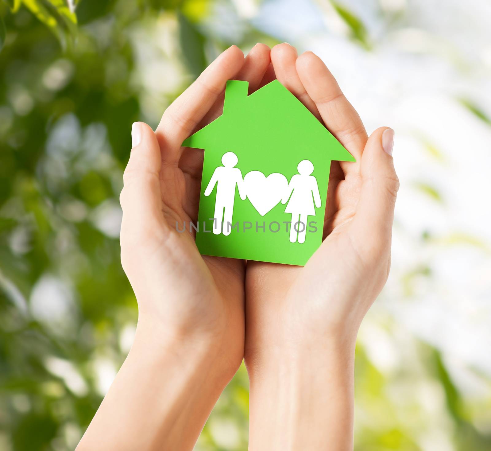 real estate and family home concept - closeup picture of female hands holding green paper house with family