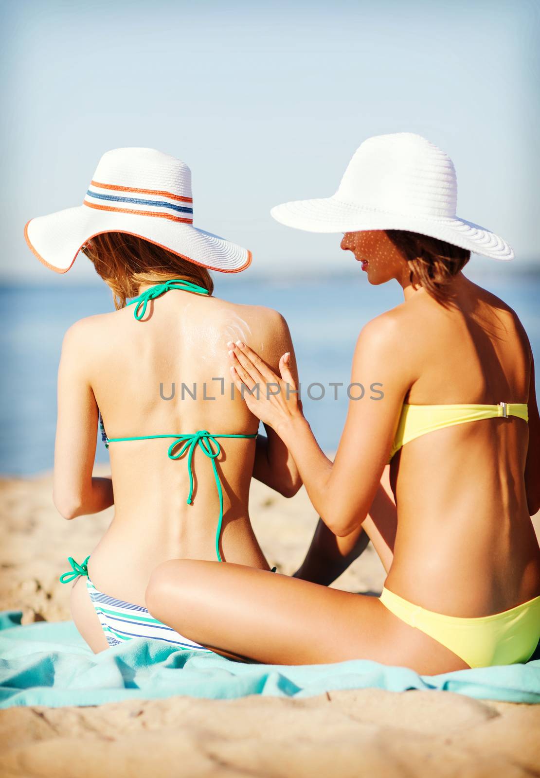 summer holidays and vacation - girls applying sun protection cream on the beach