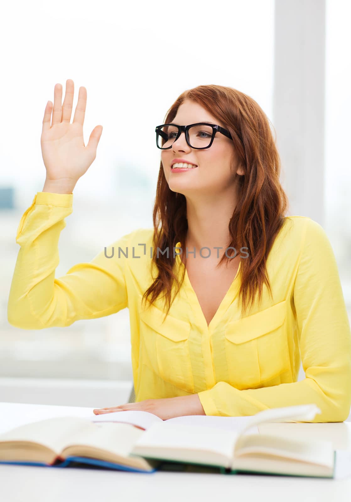 education concept - smiling student girl in eyeglasses with books and raised hand in college