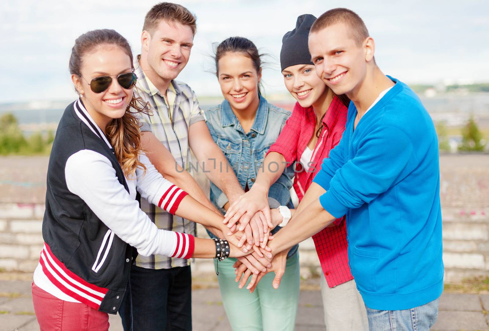 success and gesture concept - group of smiling teenagers with hands on top of each other outdoors