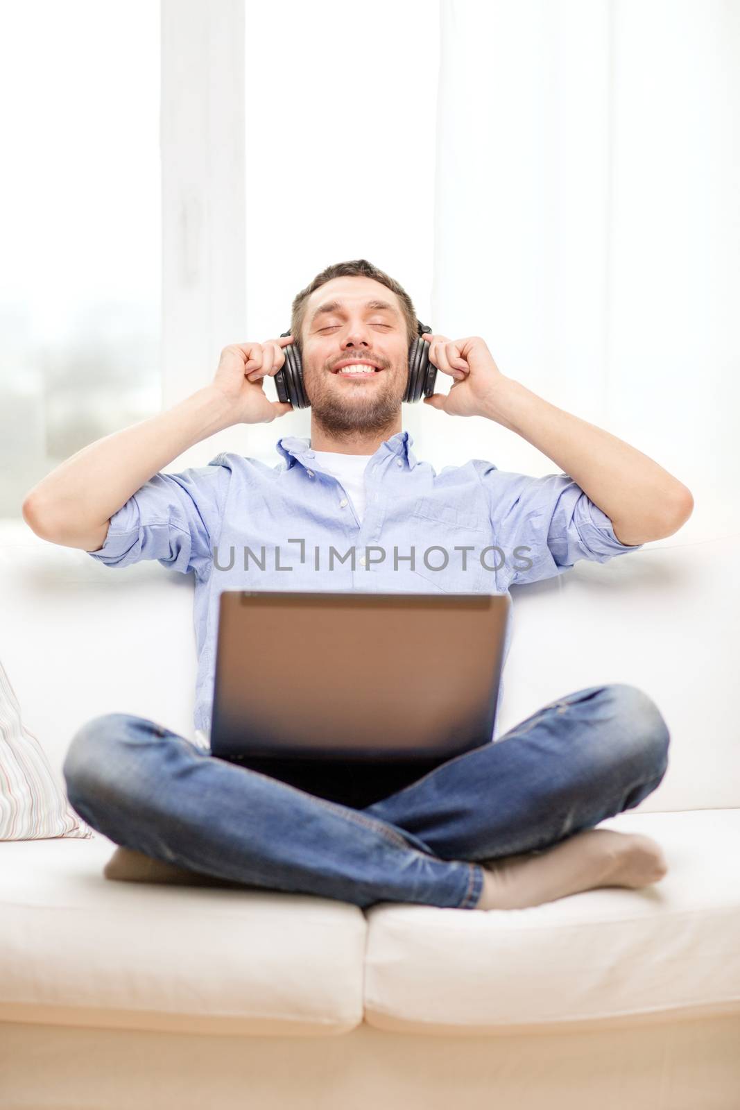 technology, home, music and lifestyle concept - smiling man with laptop and headphones at home