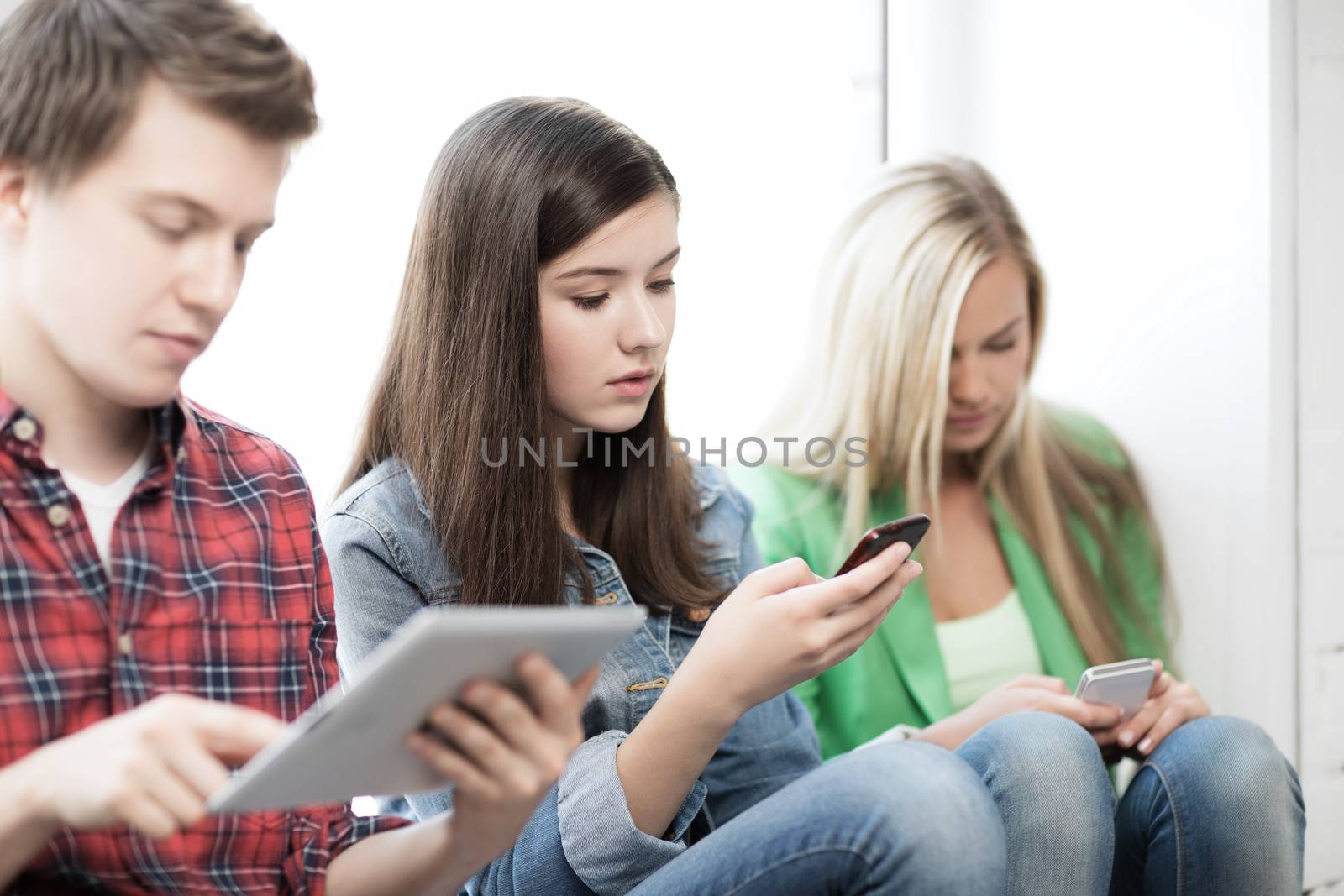 education concept - students looking into phones and tablet pc at school