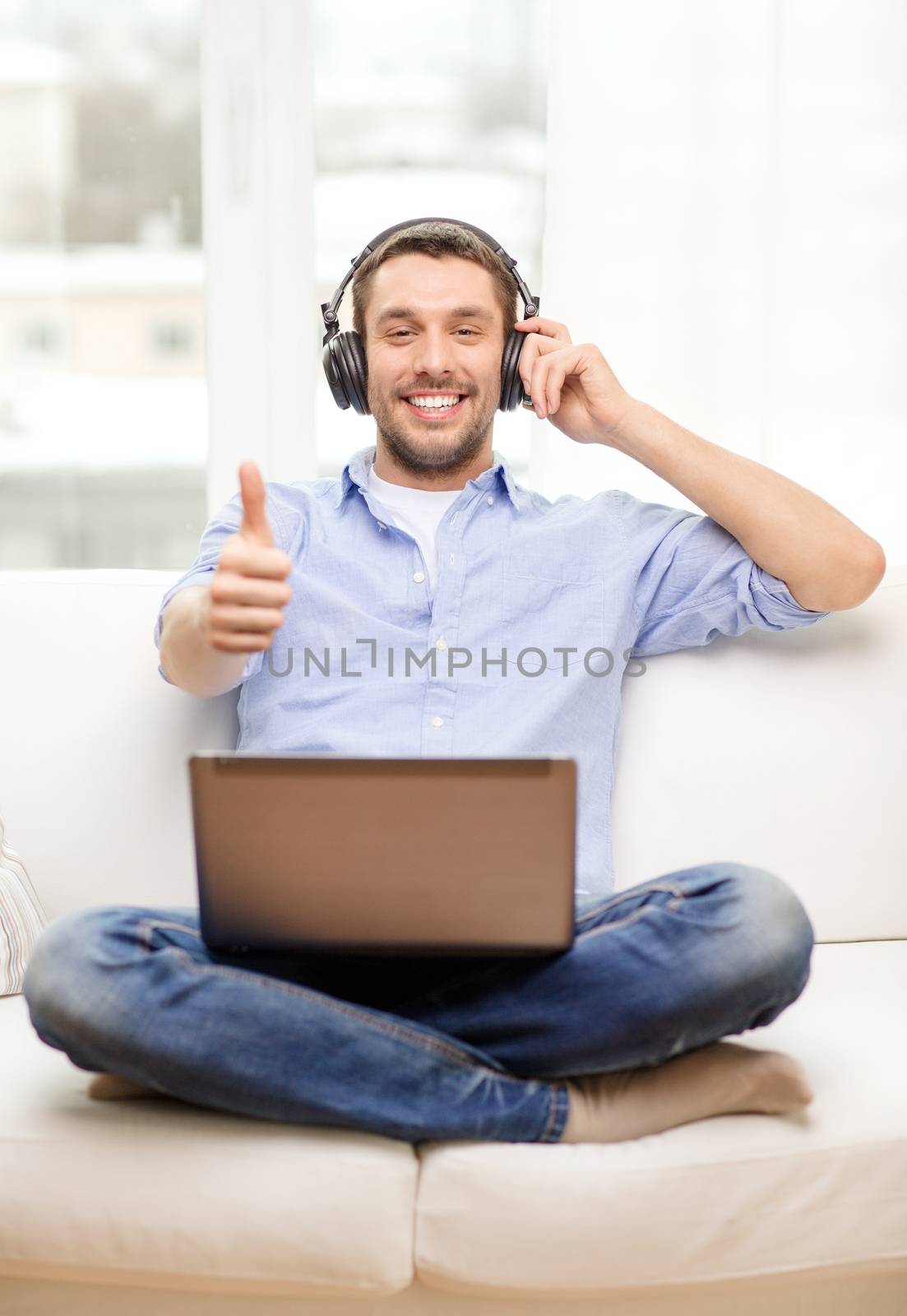 smiling man with laptop and headphones at home by dolgachov