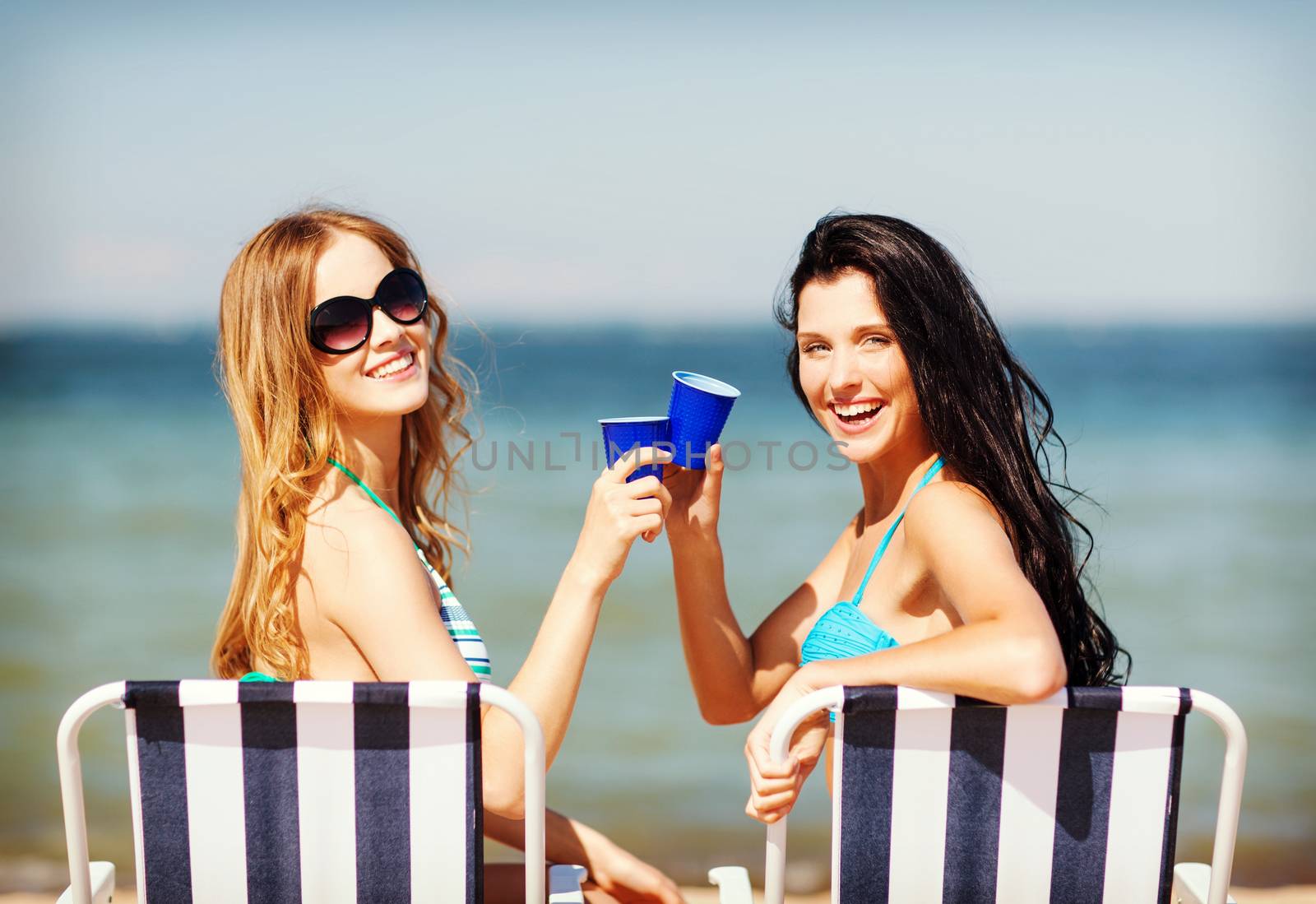 summer holidays and vacation - girls in bikinis with drinks on the beach chairs