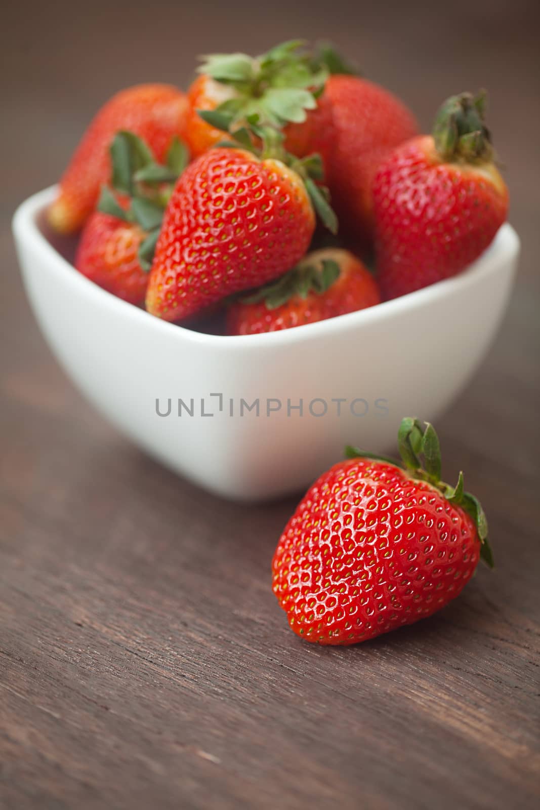red juicy strawberry in a bowl on a wooden surface by jannyjus