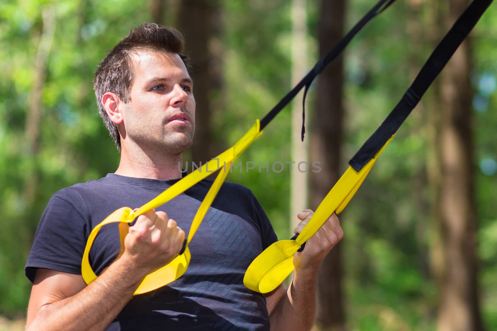 Young attractiveman does suspension training with fitness straps outdoors in the nature.