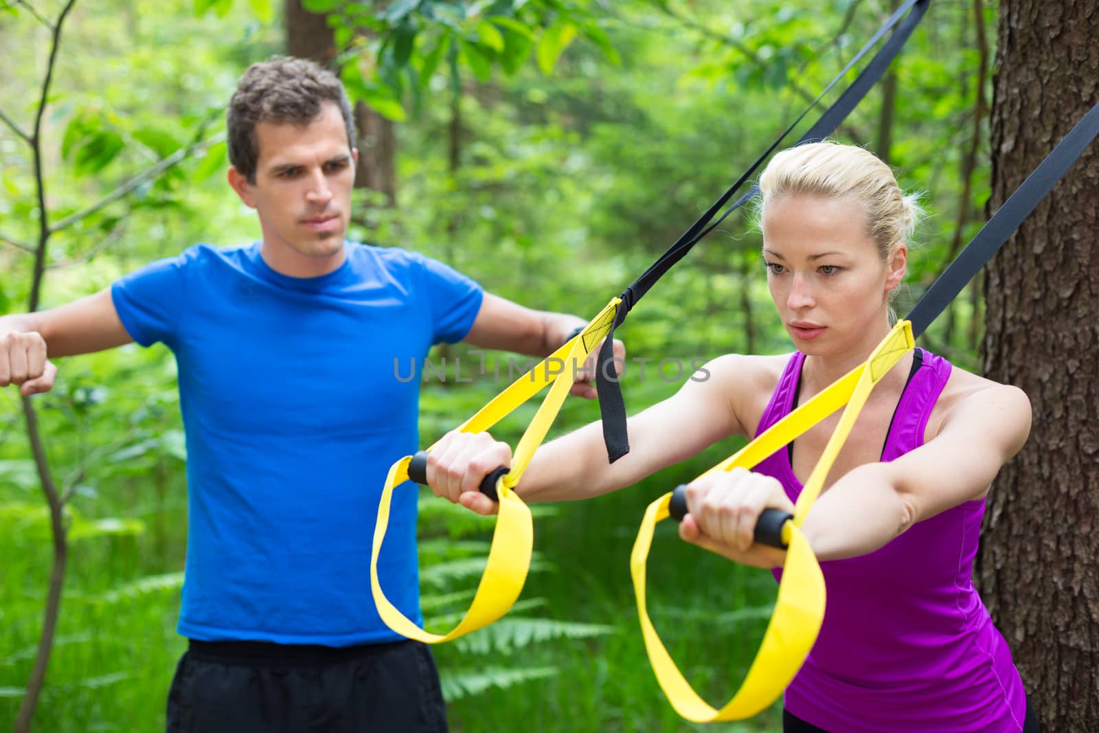 Young active people does suspension training with fitness straps outdoors in the nature.