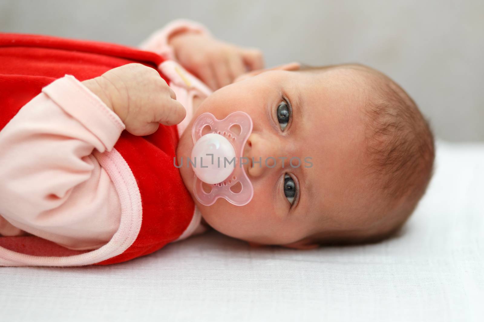 newborn, lying one month old baby in red dress with pacifier