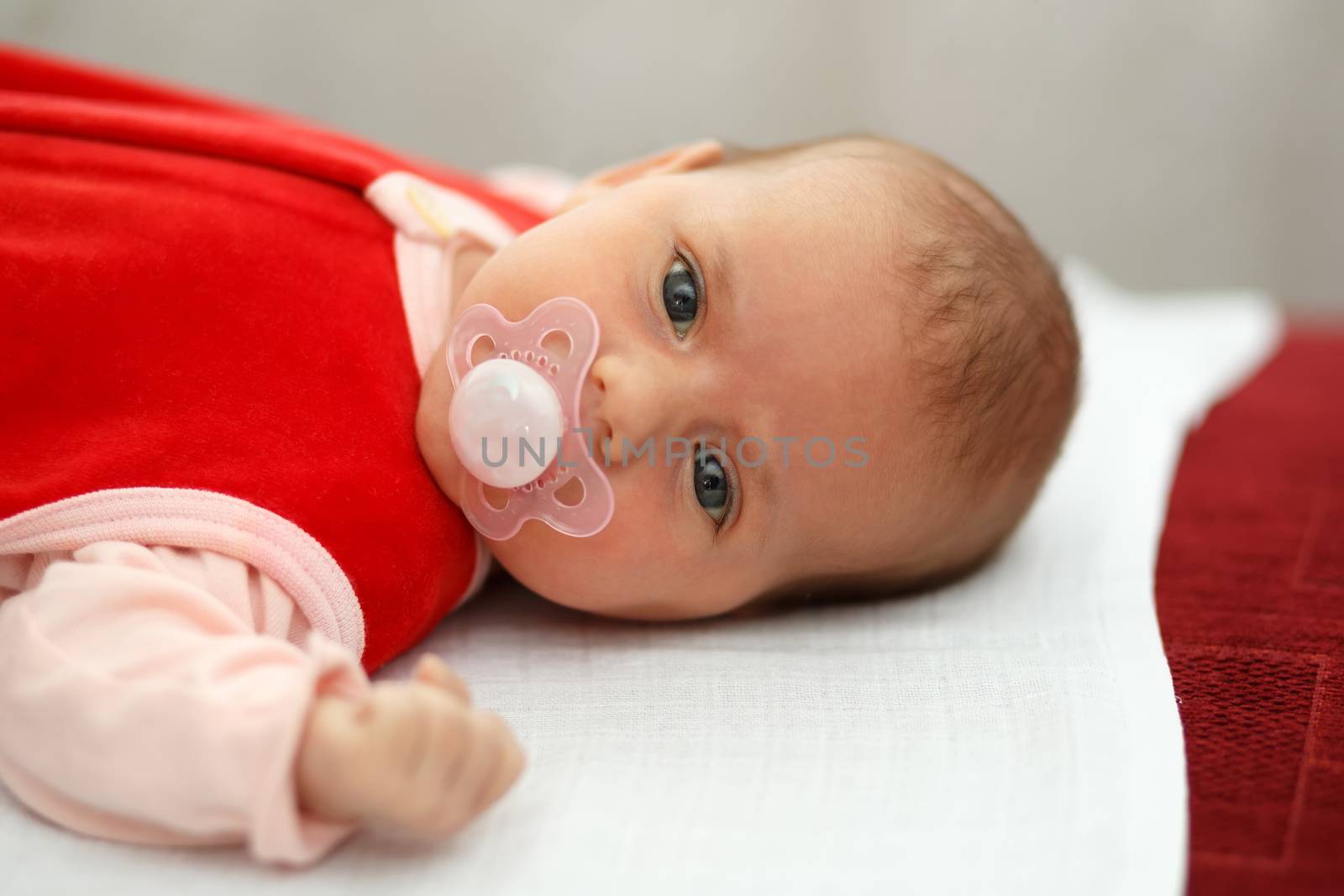 newborn, lying one month old baby in red dress with pacifier