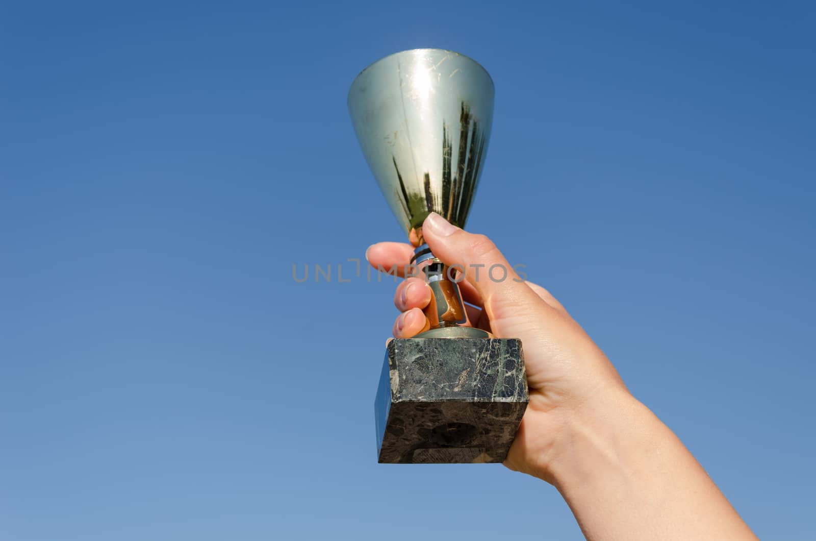 female hand hold award metallic cup on blue sky background