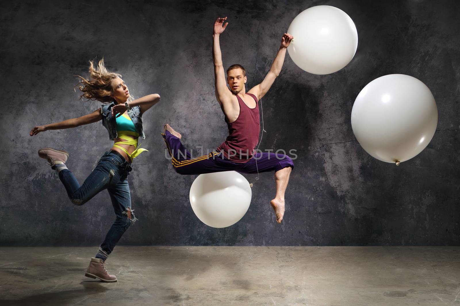A pair of dancers in a jump in the arrangement with the big balloons