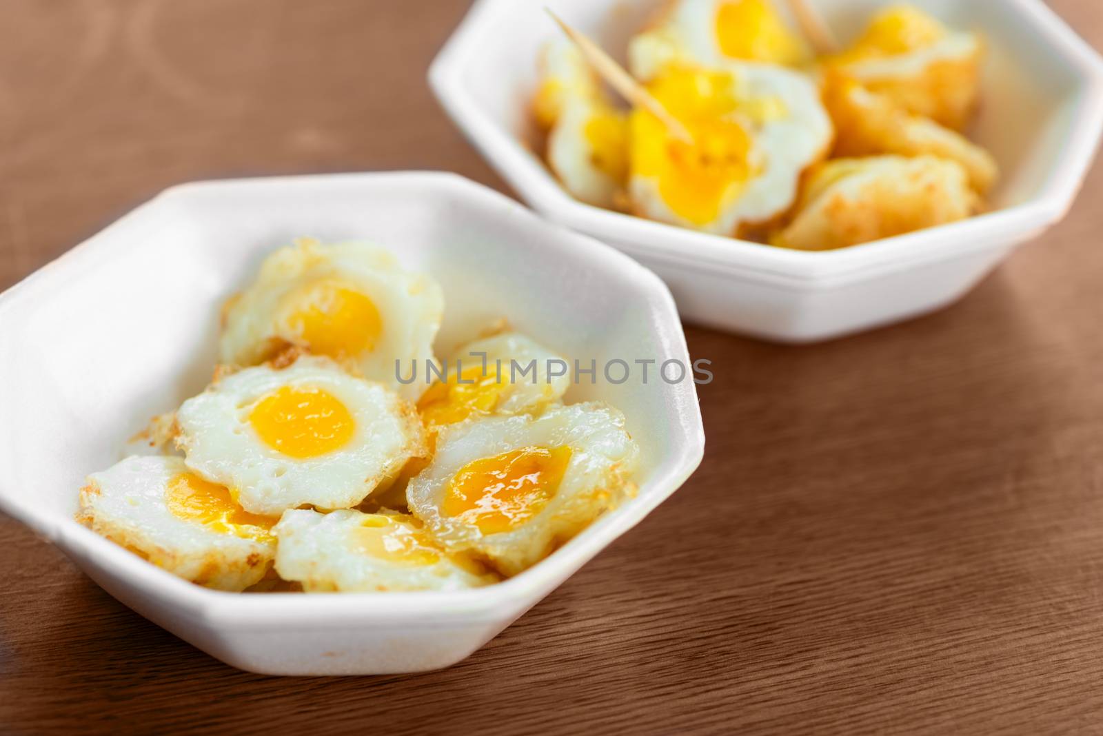 Fresh cooked fried quail eggs in white plate bowl on wooden table. Selective focus.