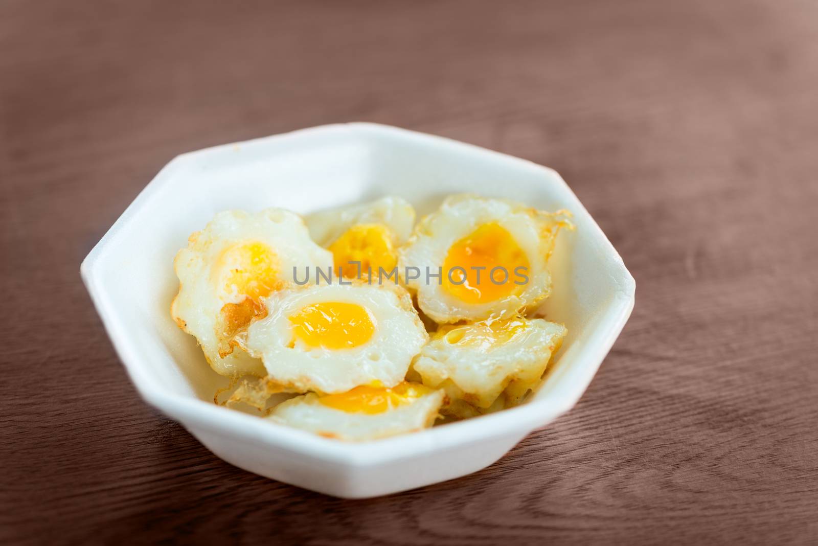 Fresh cooked fried quail eggs in white plate bowl on wooden table. Selective focus.