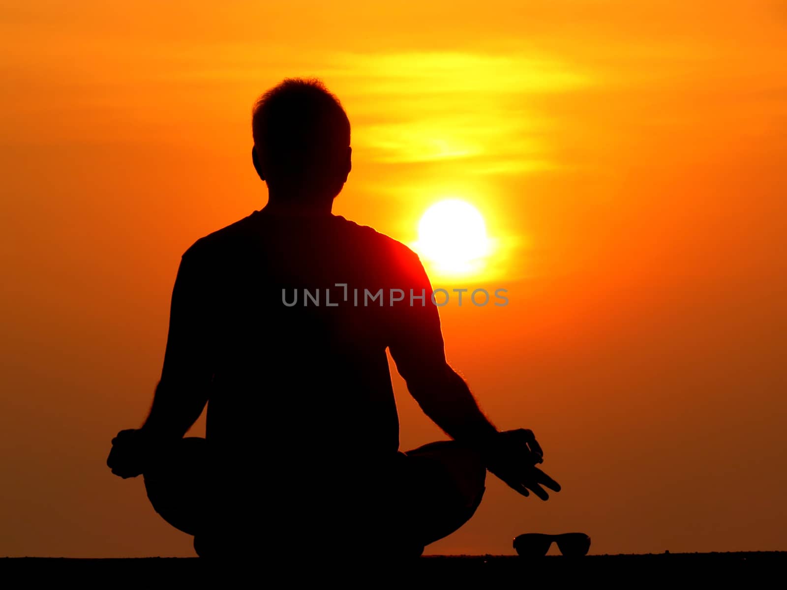 A man keeping aside his sunglasses aside and meditating on the rising sun on a spiritual holiday