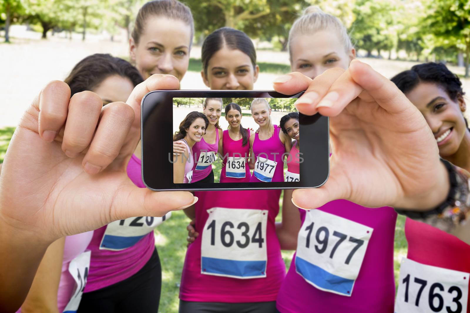 Hand holding smartphone showing confident female participants of breast cancer marathon