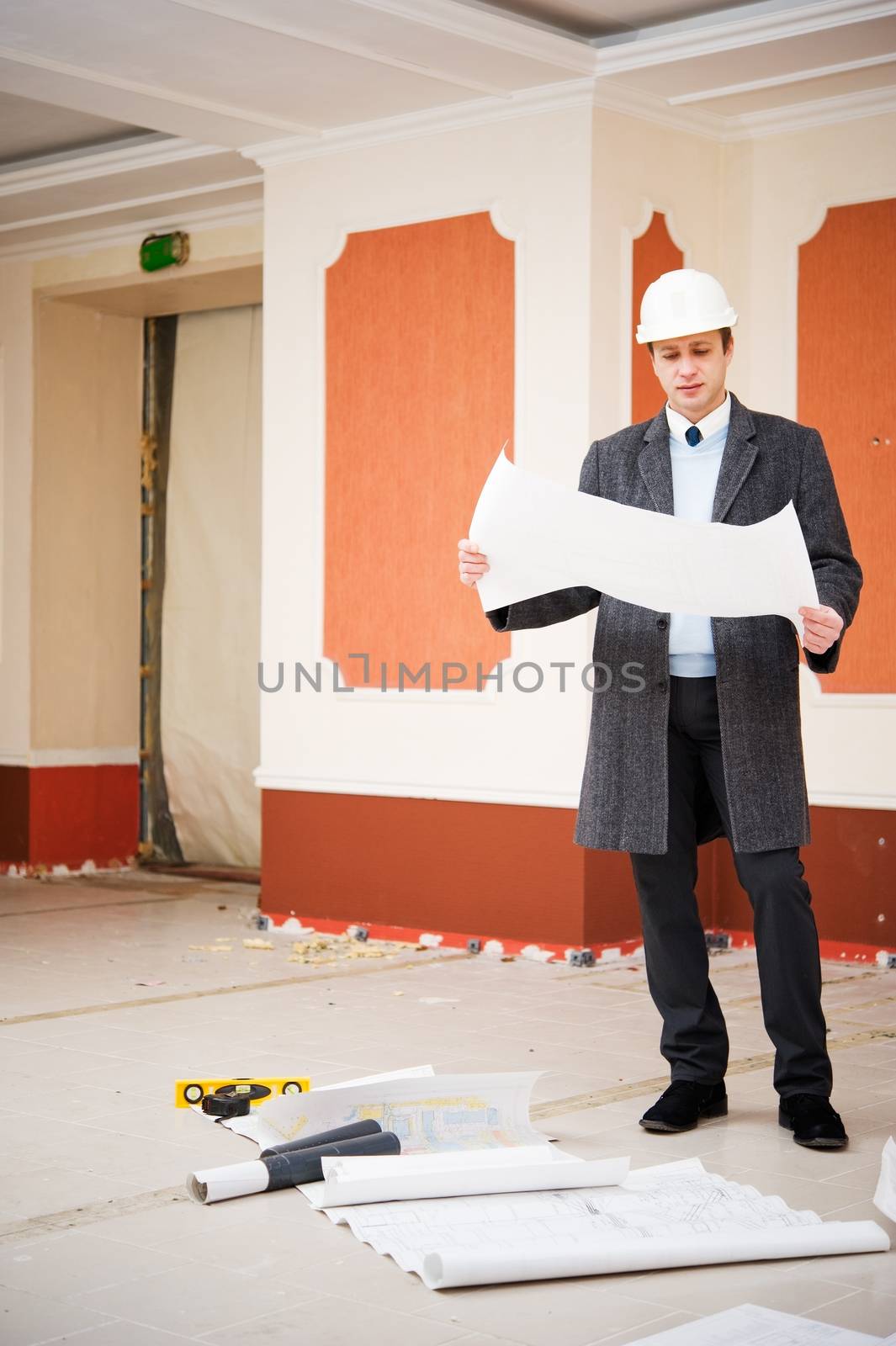 Engineer or architect in the white hard hat with the blueprint. Reconstruction interior.