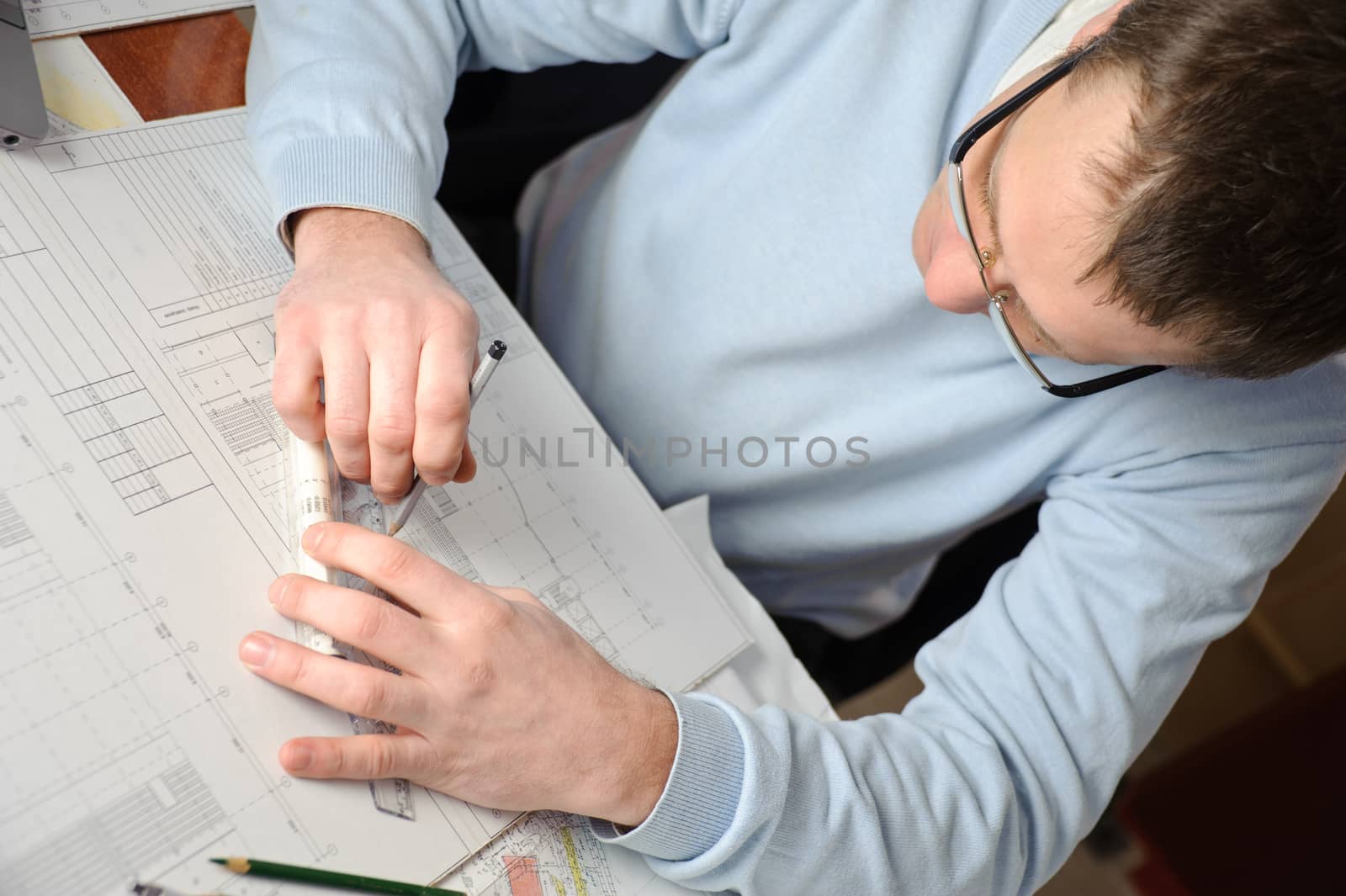 Engineer or architect in blue pullover is working on construction plans.