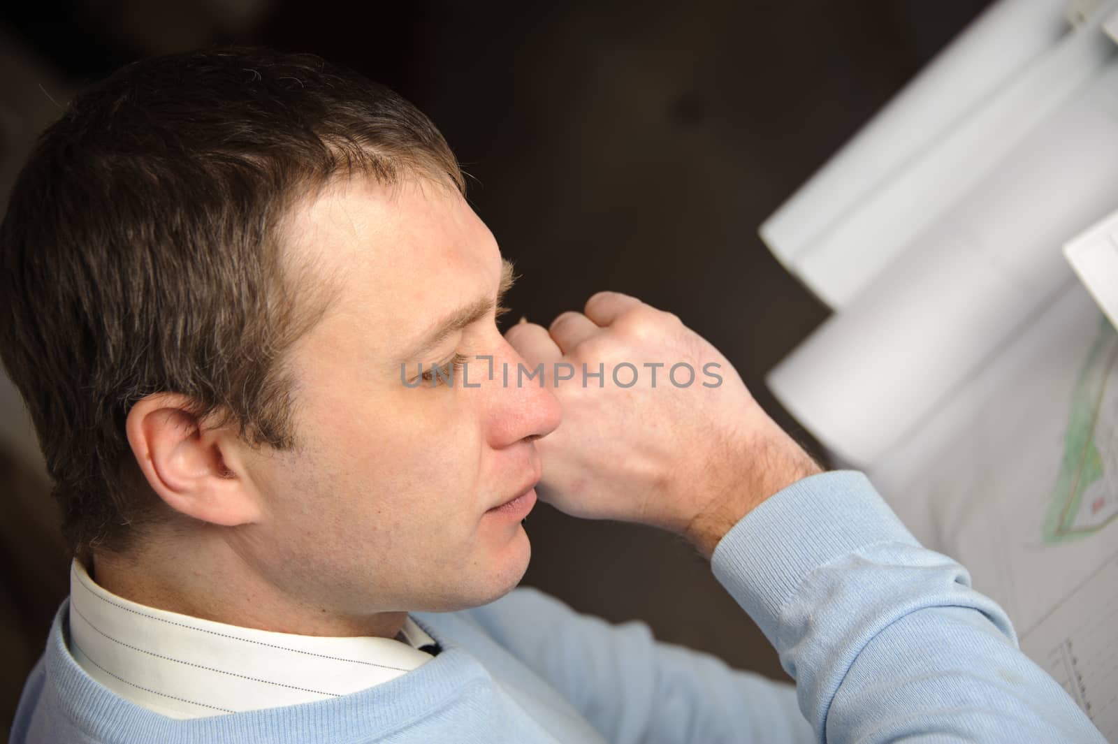 Portrait of engineer or architect in blue pullover is working on construction plans.