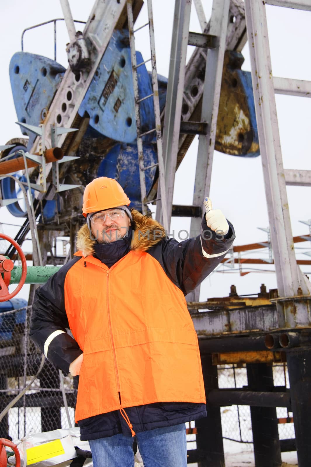 Oil worker in orange uniform and helmet on of background the pump jack.