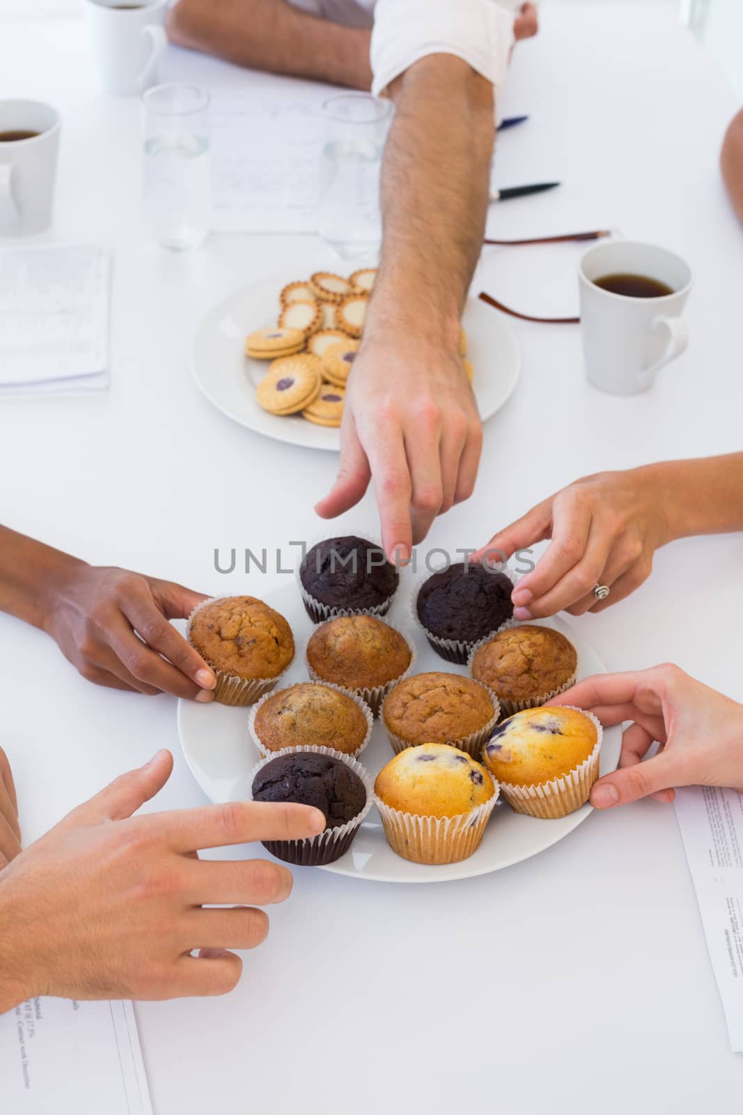 Business people taking muffins from plate in the office