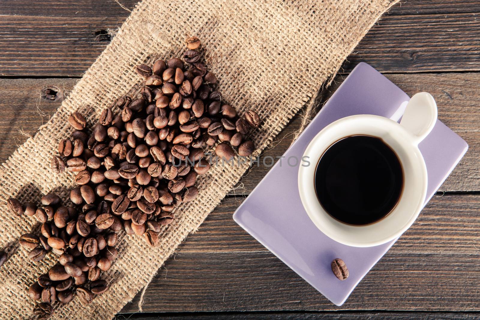 cup of black coffee with some coffee beans scattered on wooden table. point of view from below