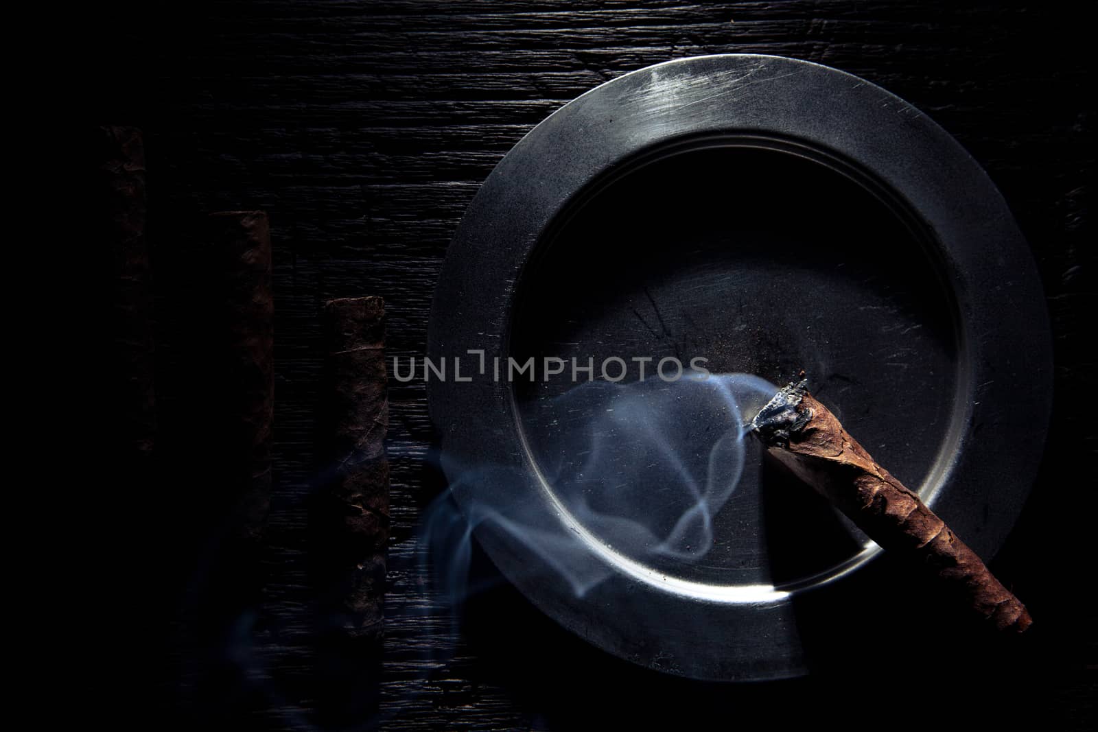 geometric composition of cigars end ashtray. the cigar is lit and it's steaming.