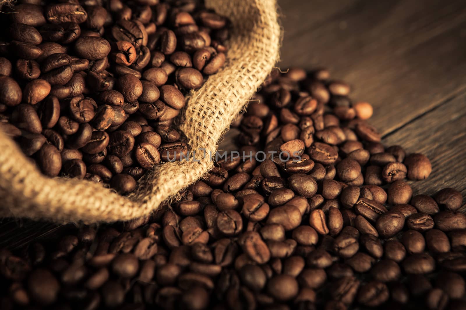 close up of jute bag full of coffee beans, and some coffee beans scattered on a wooden table