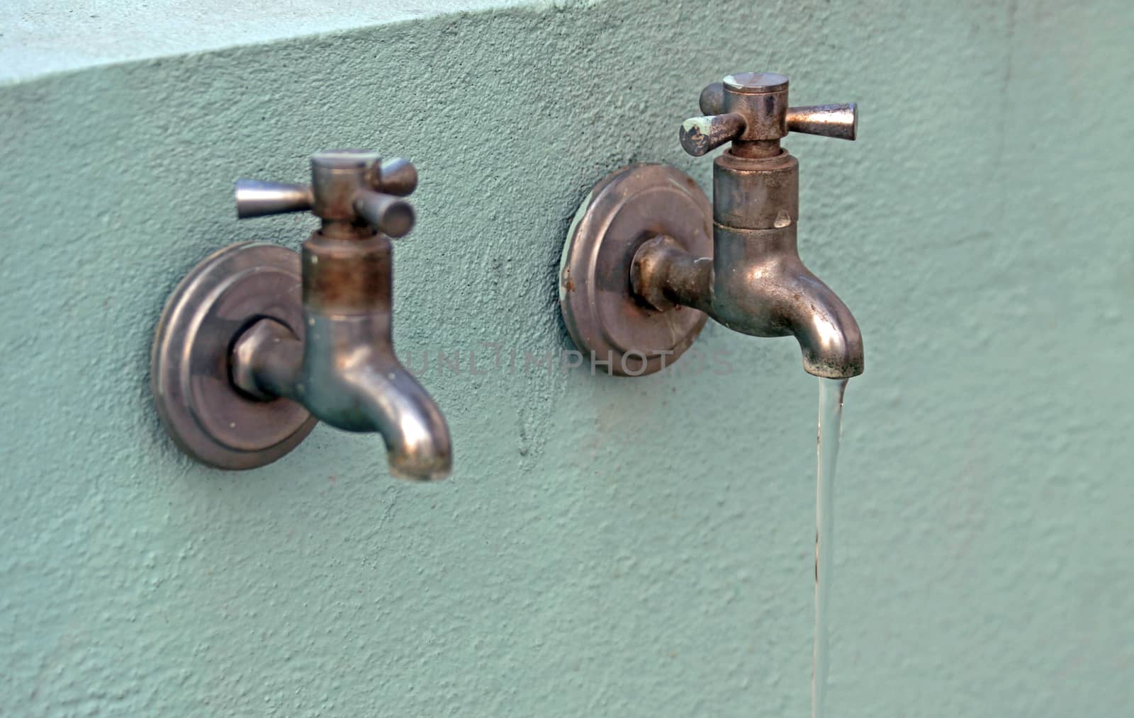 two discolored rusty taps are seen on a wall with water flowing from one