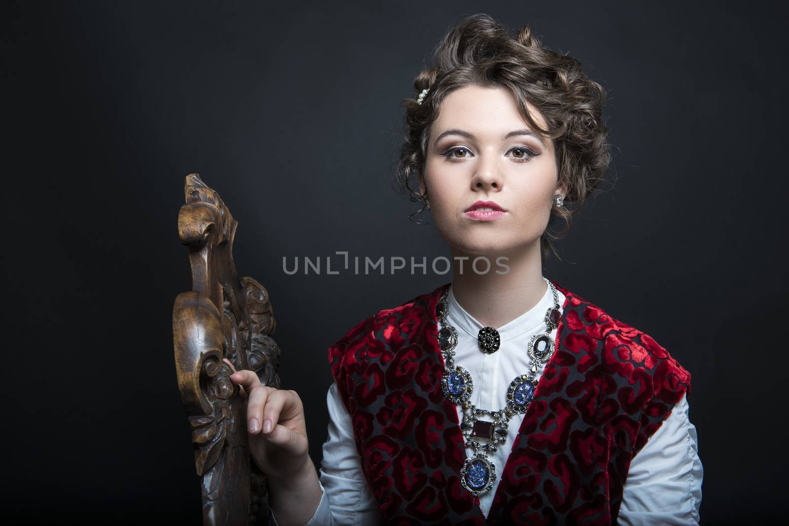 Portrait of beautiful Caucasian model in red Victorian-style velvet dress, seated on wooden chair