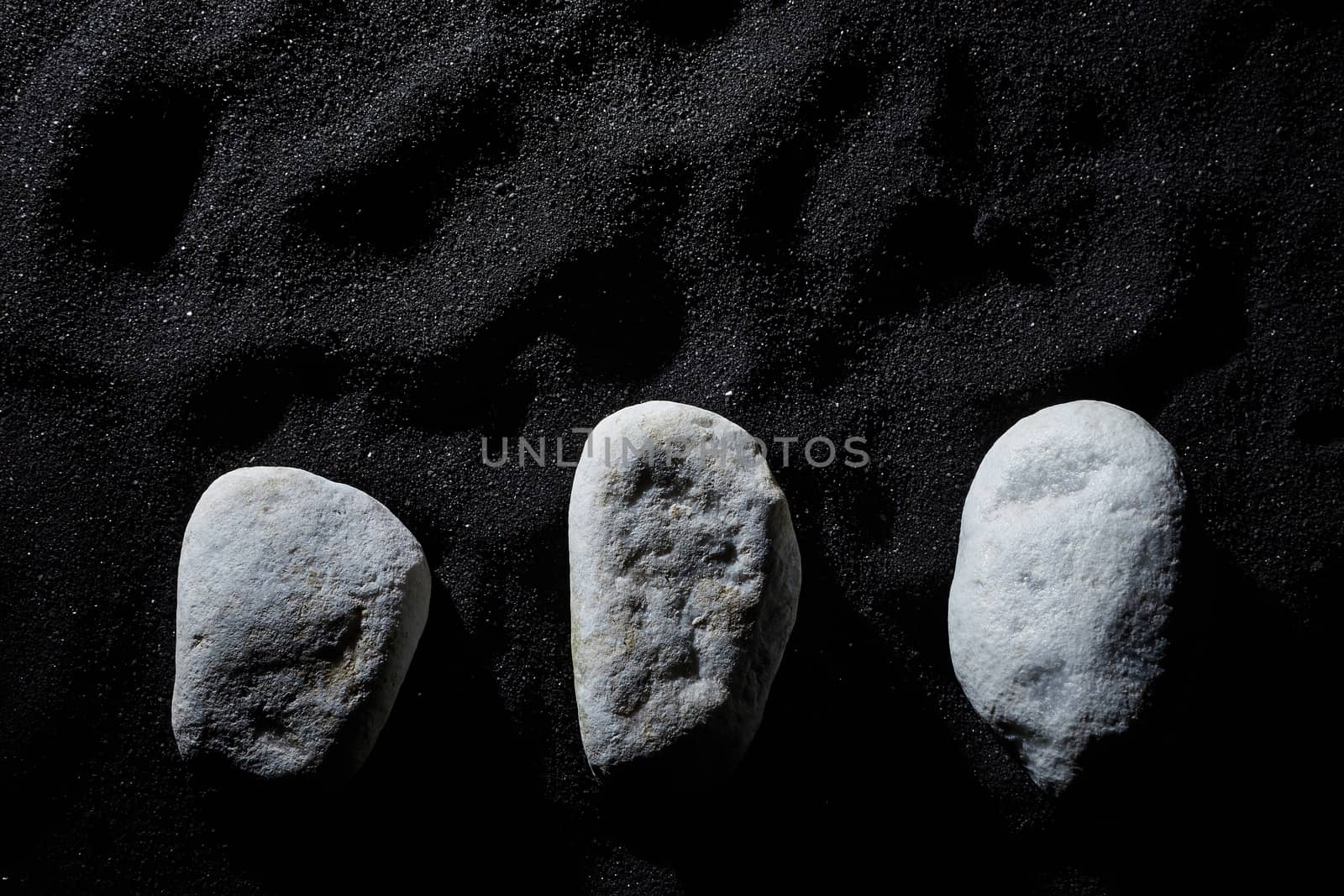 three white stones on black sand