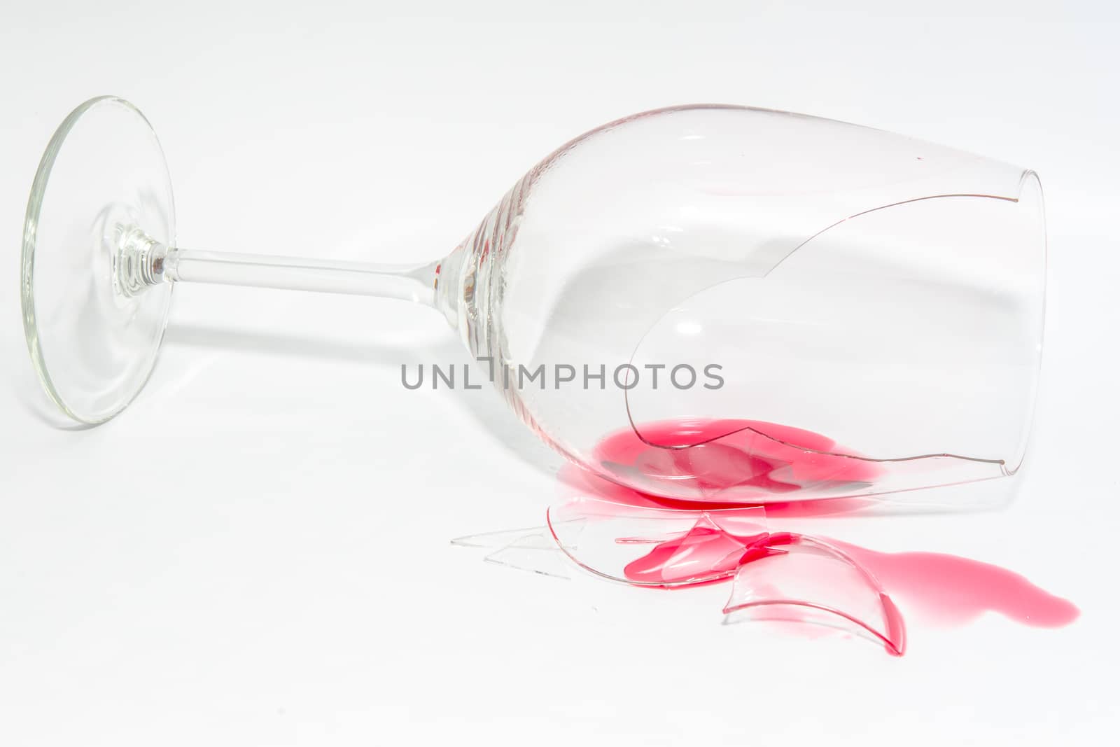 Shattered snifter glass with splattered spilt red wine and sharp splinters on background