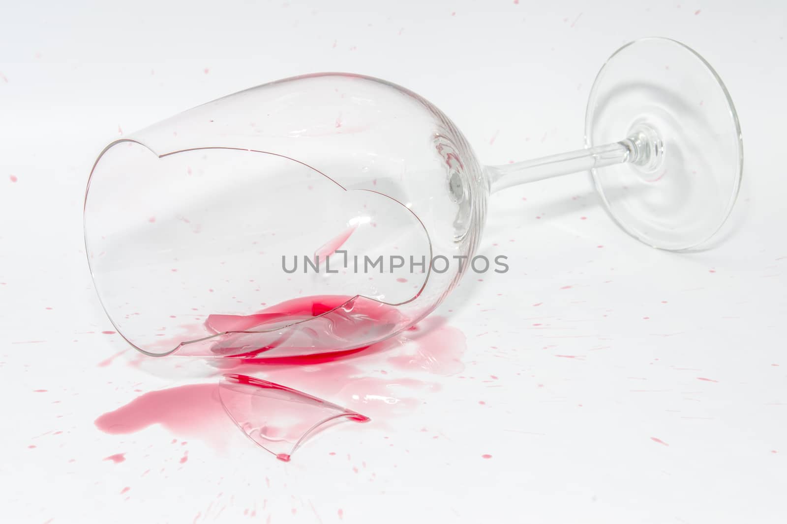 Broken wineglass with sharp shards and spilled splash of red wine on white background