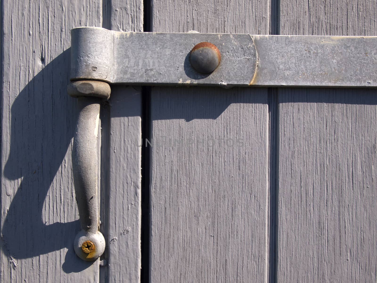 Closeup view of an old vintage metal hinge on a gray wooden door