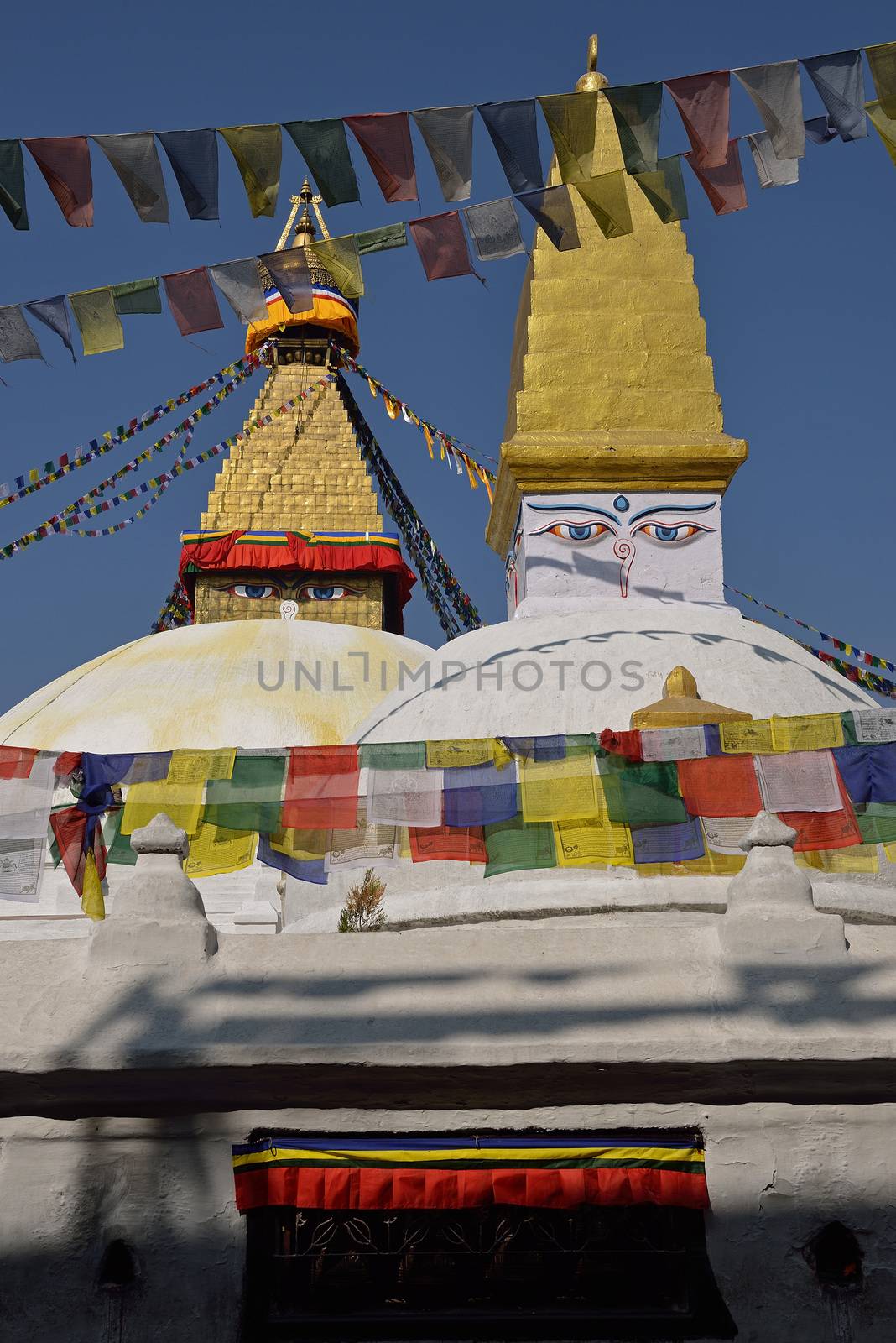 Boudhanath Stupa. Golden spire and all seeing Buddha eyes on top a giant white hemisphere. Smaller stupa in foreground. Kathmandu, Nepal