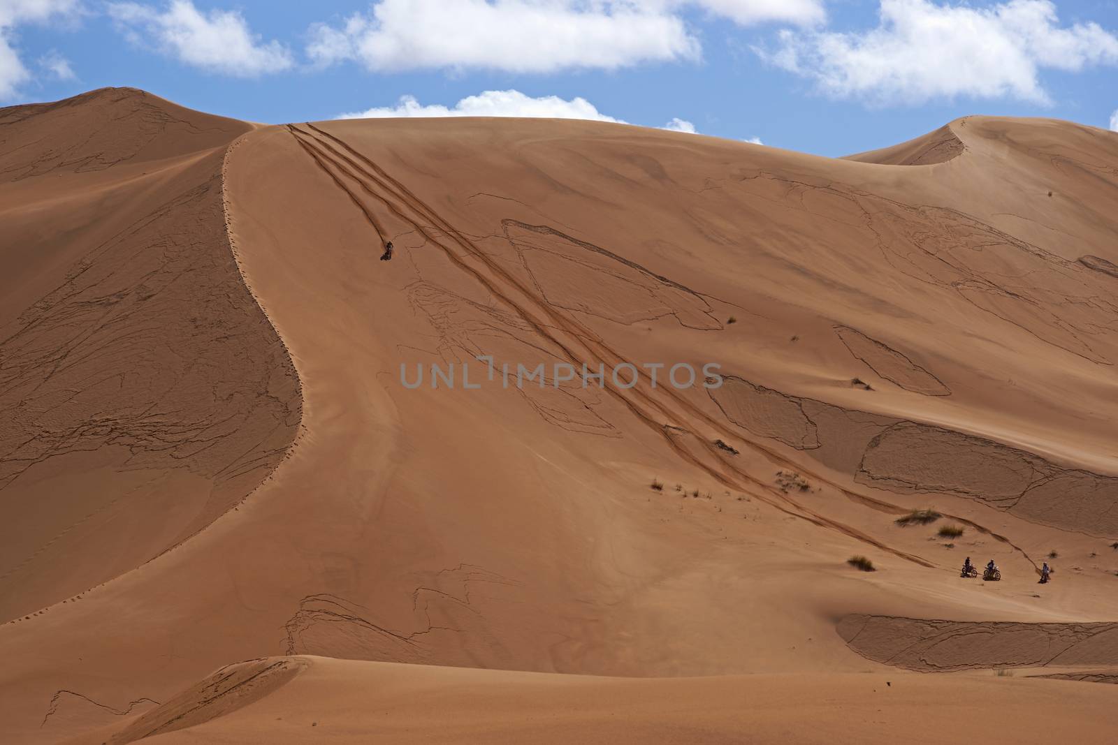 Group of bikers descend a steep sand dune in the Sahara Desert of Morocco in North Africa