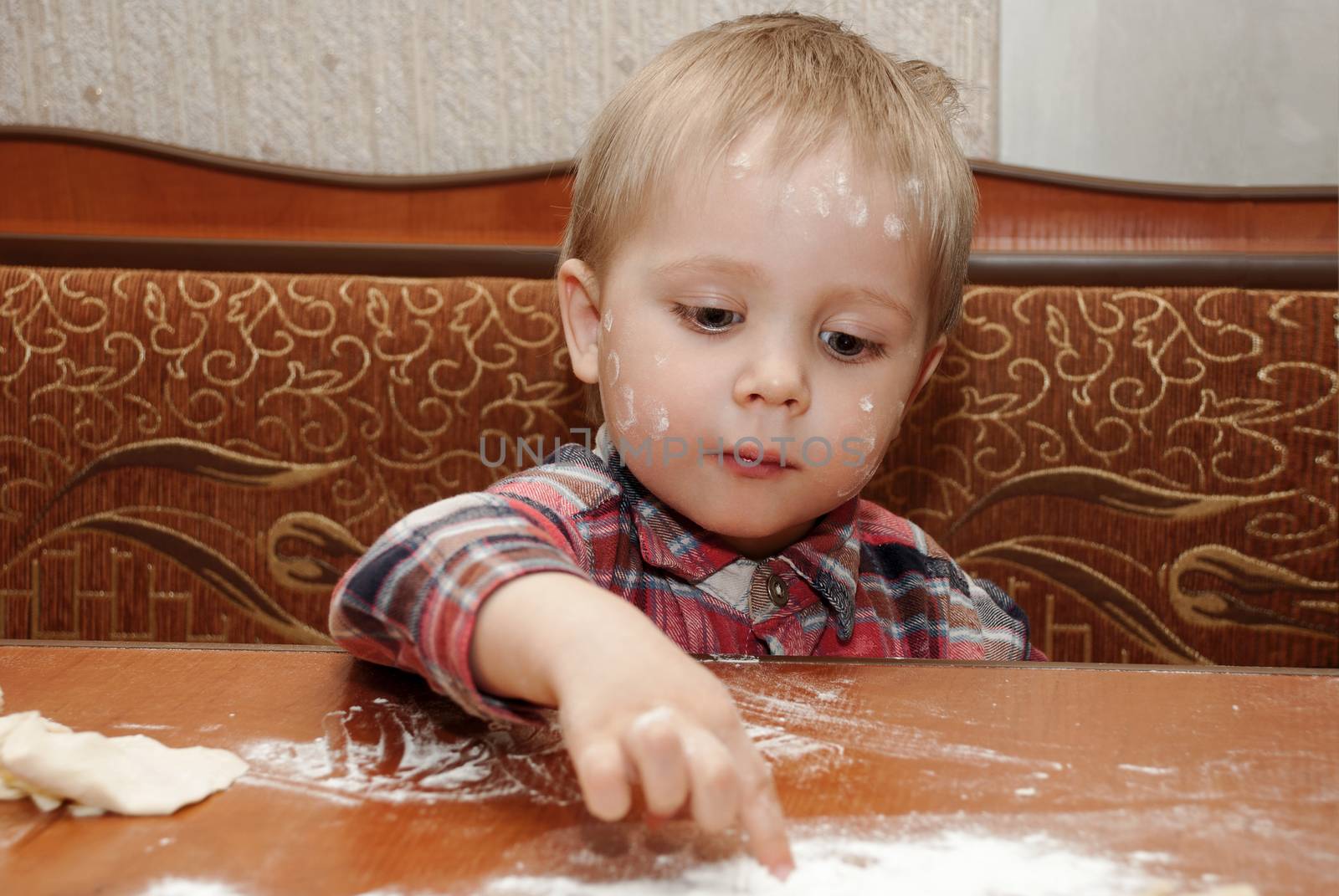 Little funny boy in the kitchen engaged in cooking