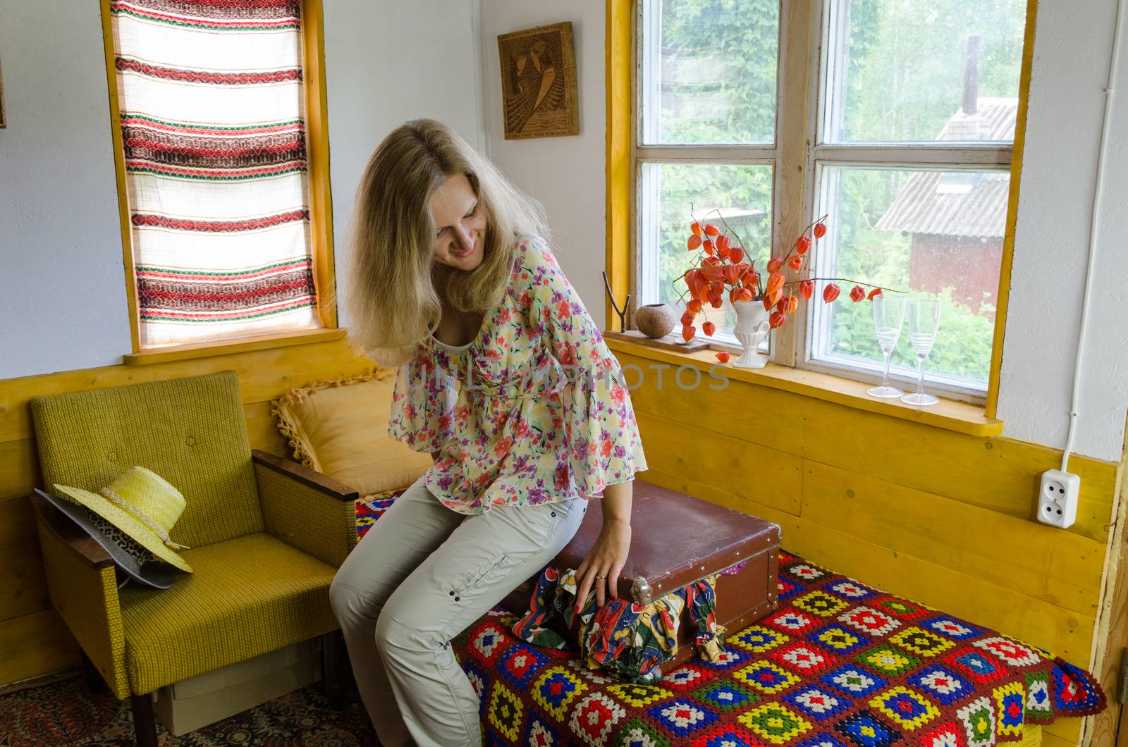 smiling young woman sitting on overstuffed suitcase in bed rural room