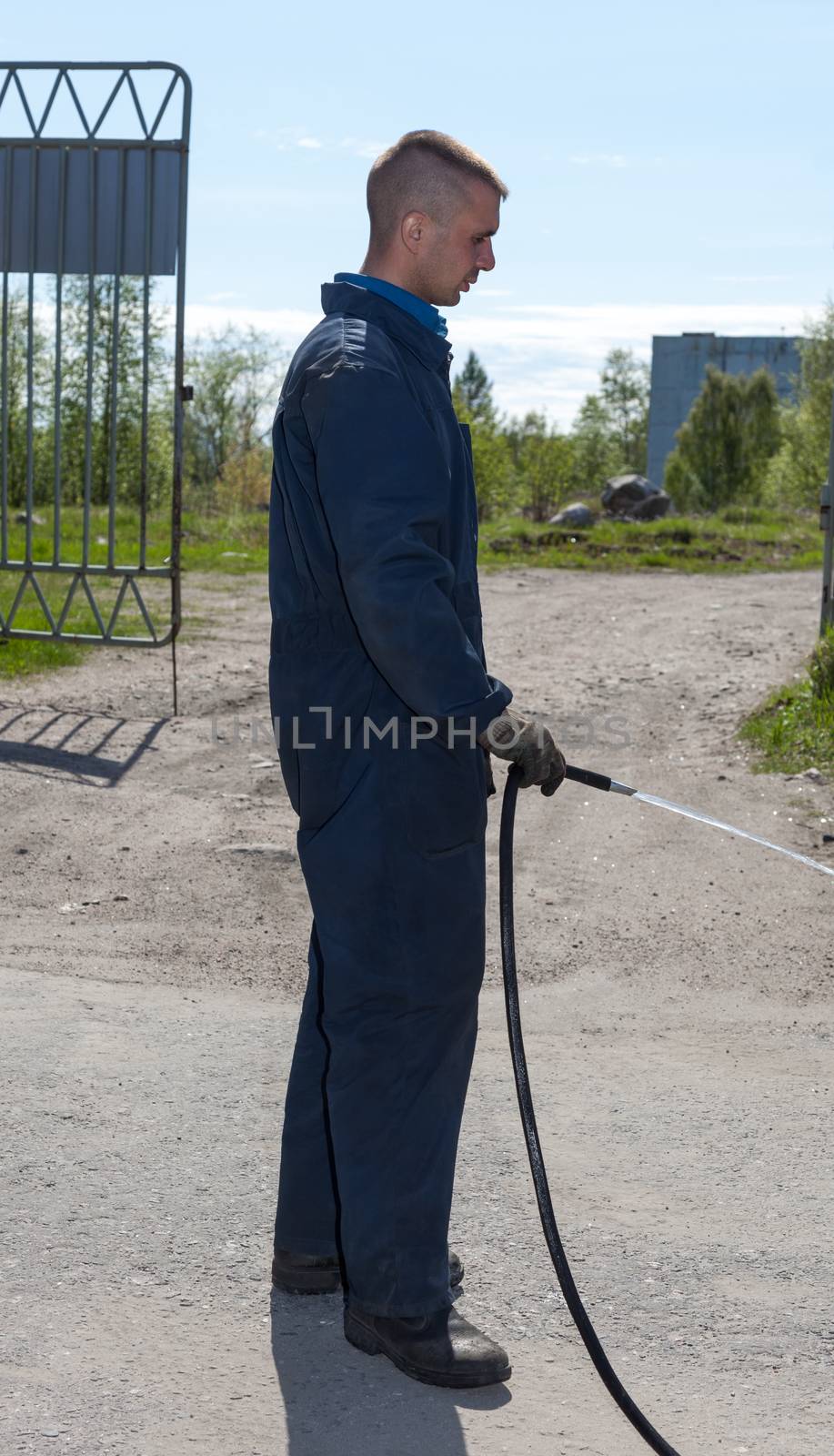 Worker in overalls watering area with water from a hose. covered space 