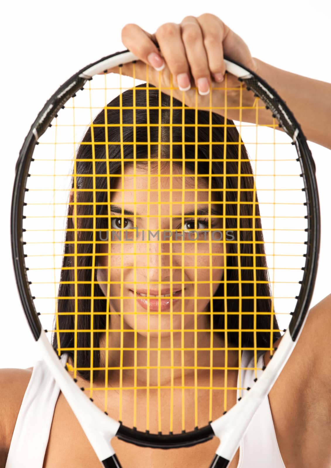 Young female tennis player looking through strings of racket over white