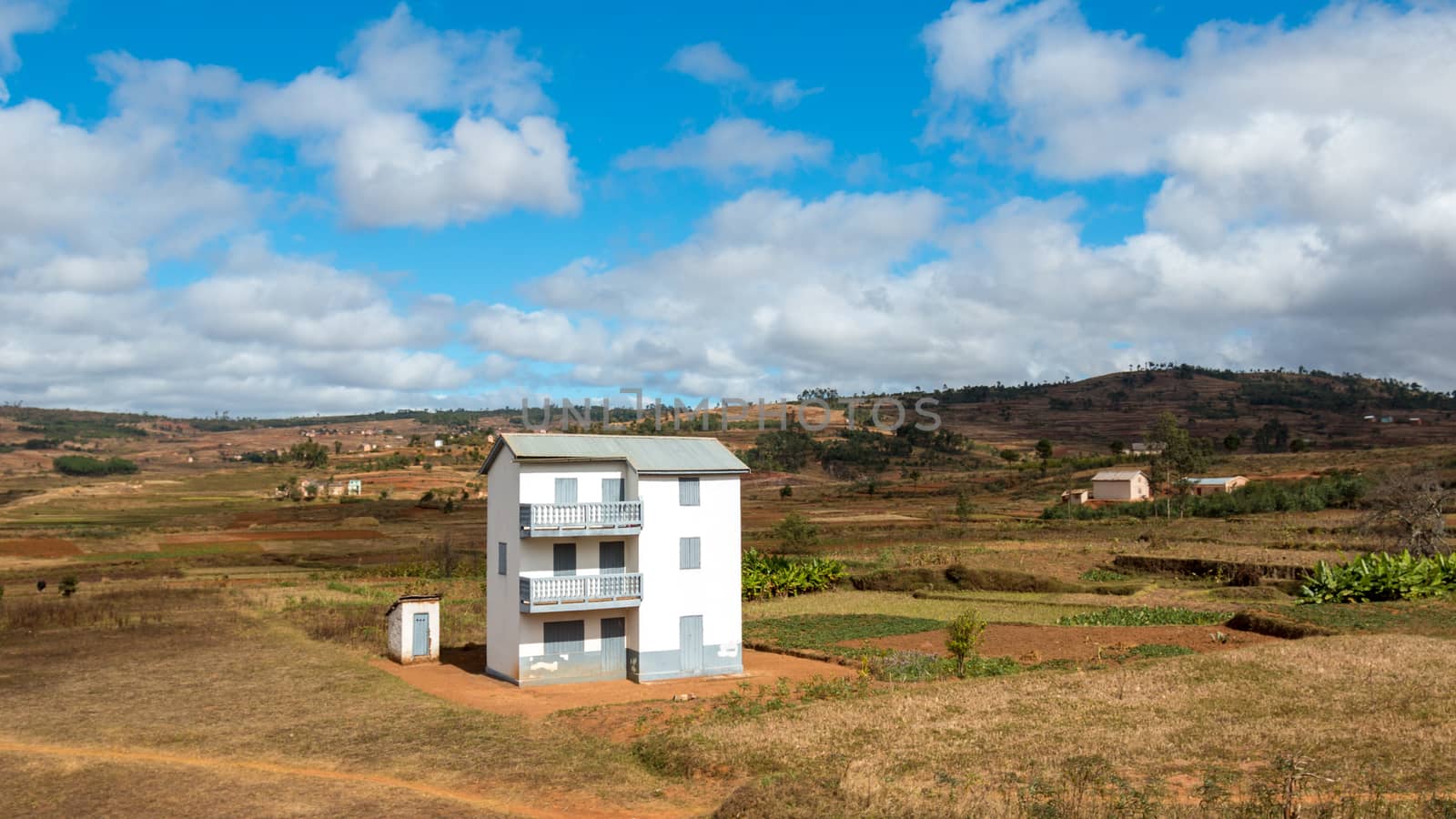 A two story white house next to a small white house in the middle of a beautiful landscape in Madagascar