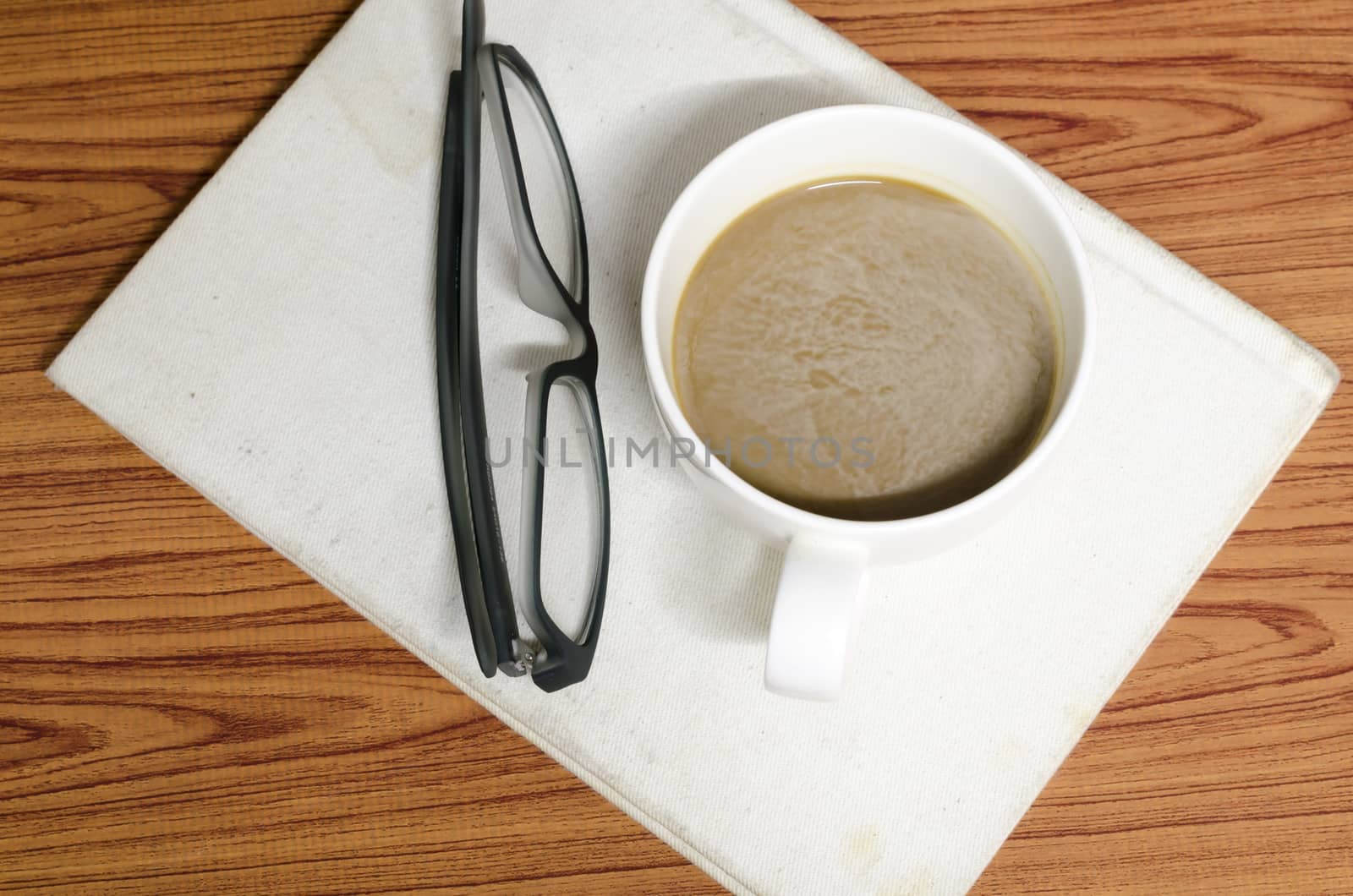 coffee cup and notebook with glasses on wood background