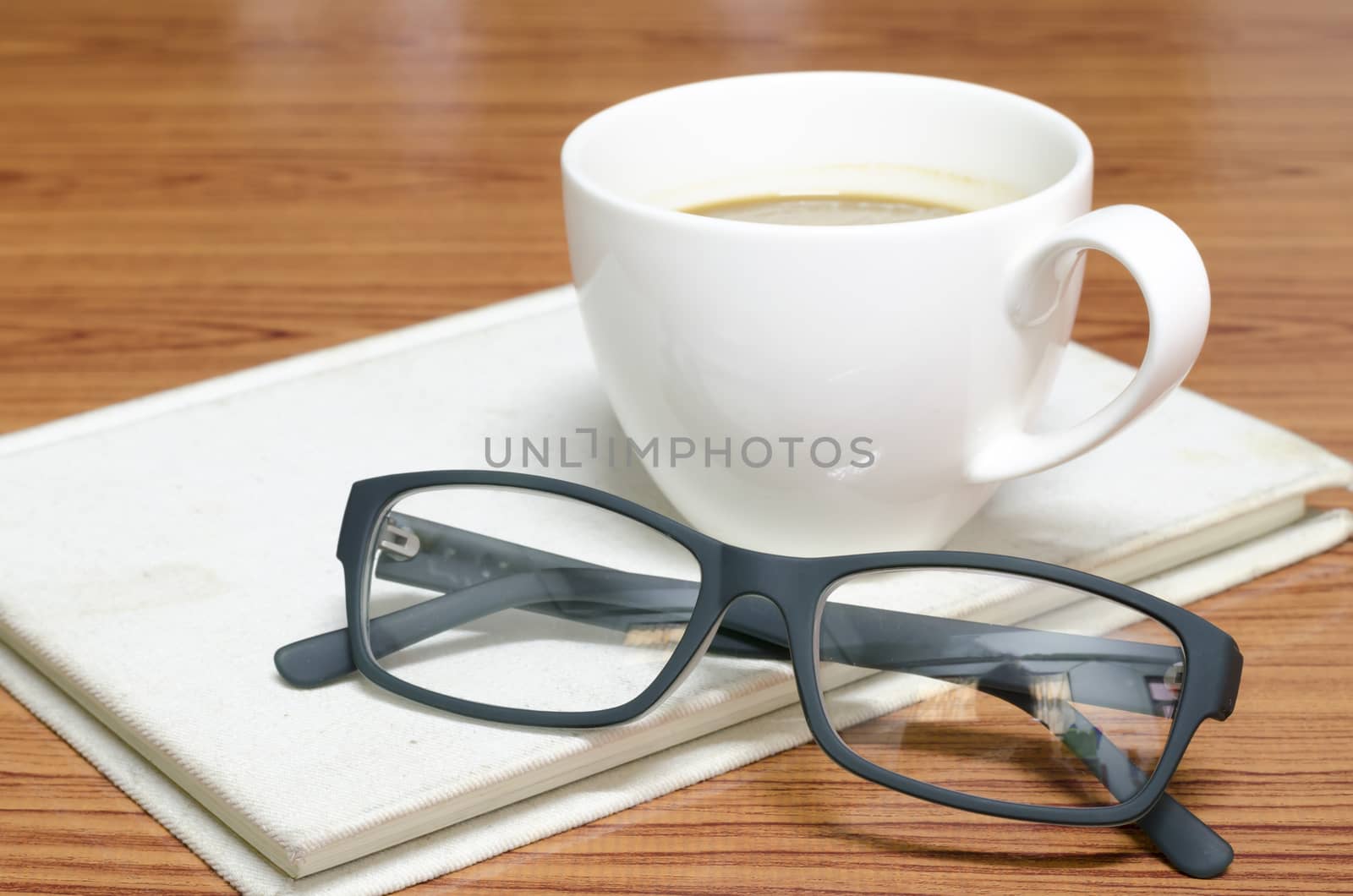 coffee cup and notebook with glasses on wood background