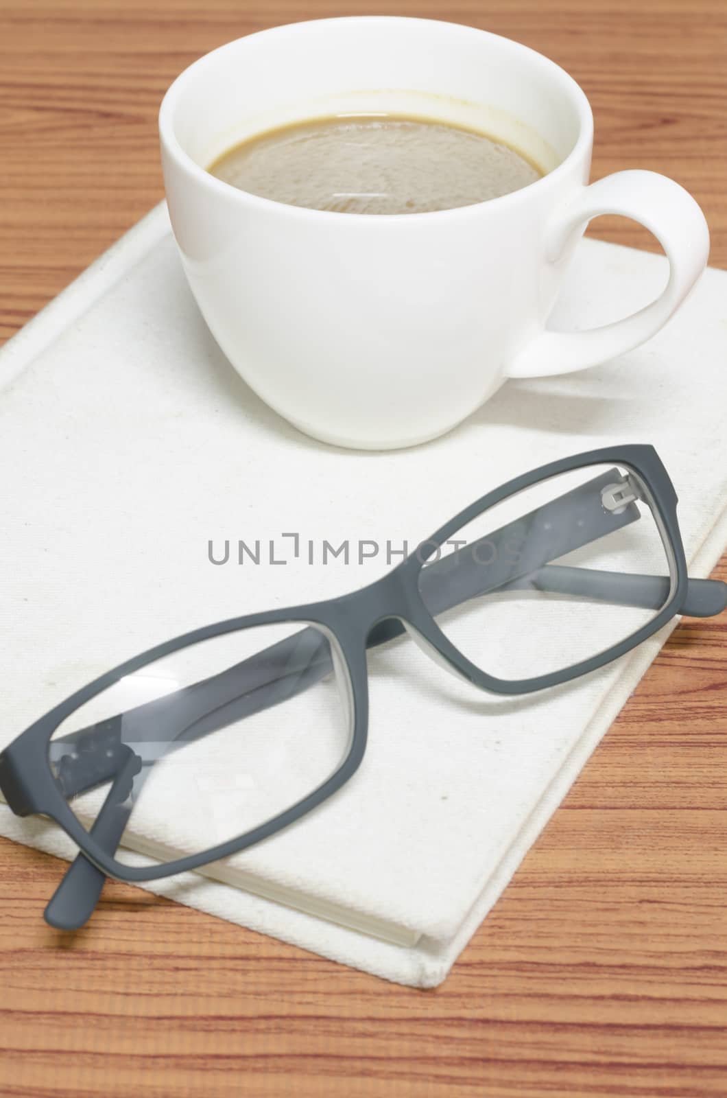 coffee cup and notebook with glasses on wood background