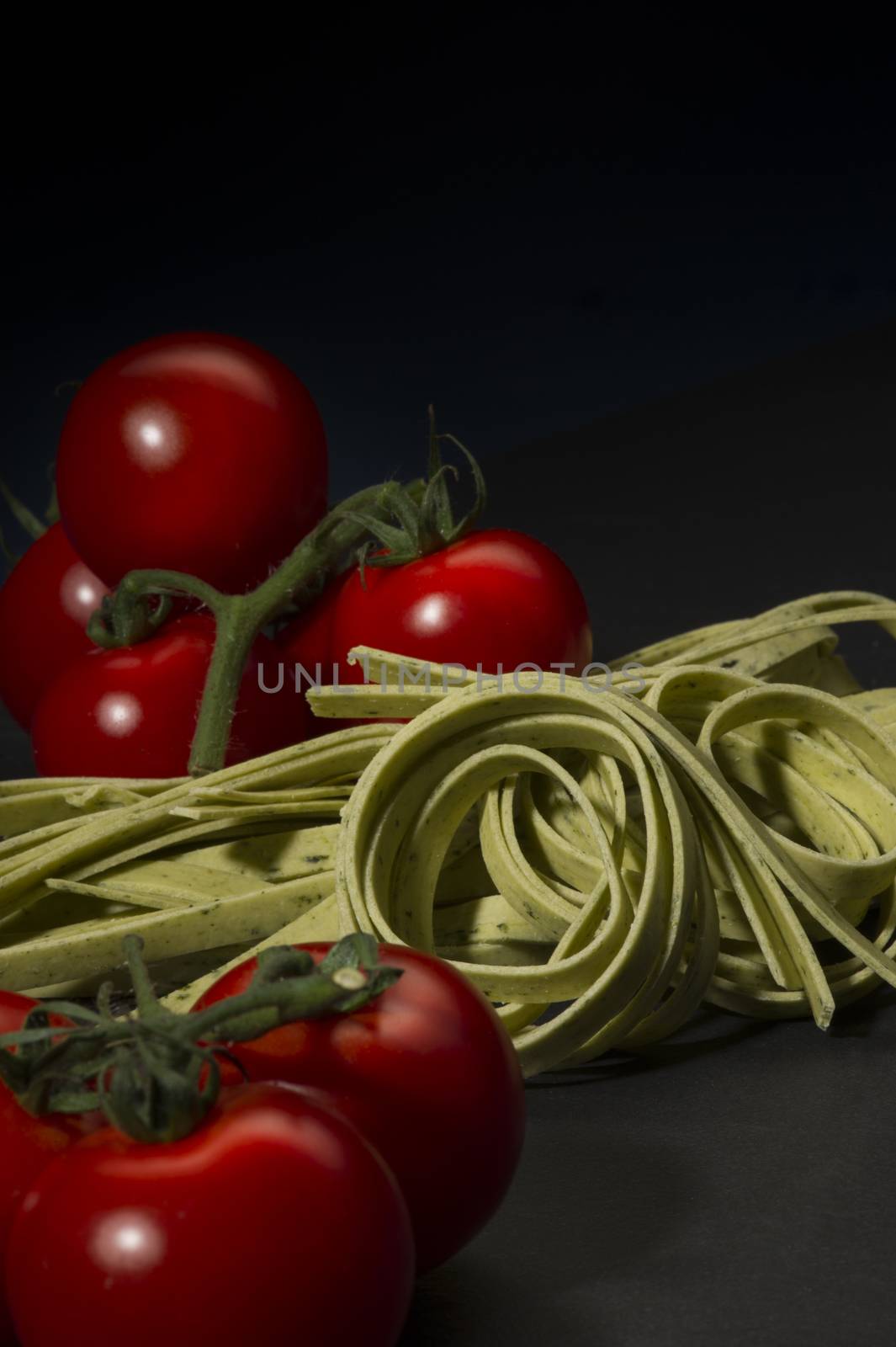 Dried tagliatelle pasta and ripe cherry tomatoes standing ready to be cooked on a rustic kitchen counter for a traditional Italian pasta dish, vertical format on a dark background with copyspace