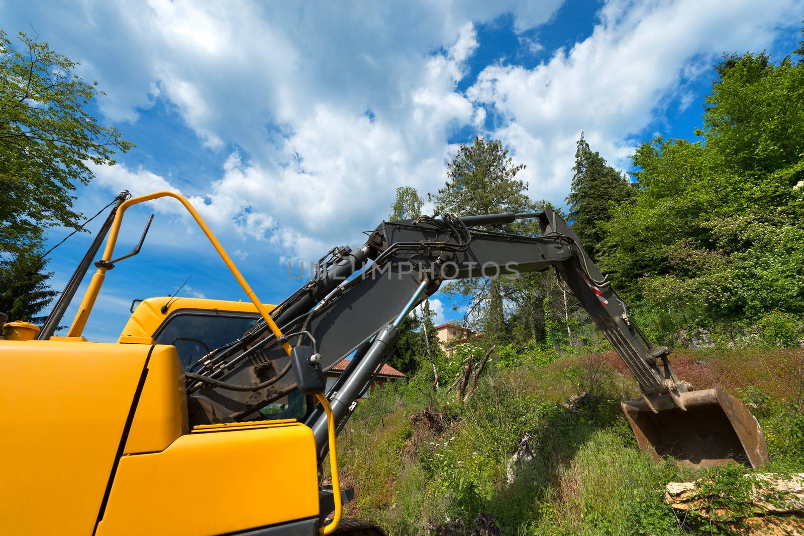 Close up of tracked excavator yellow and black at woods and blue sky with clouds