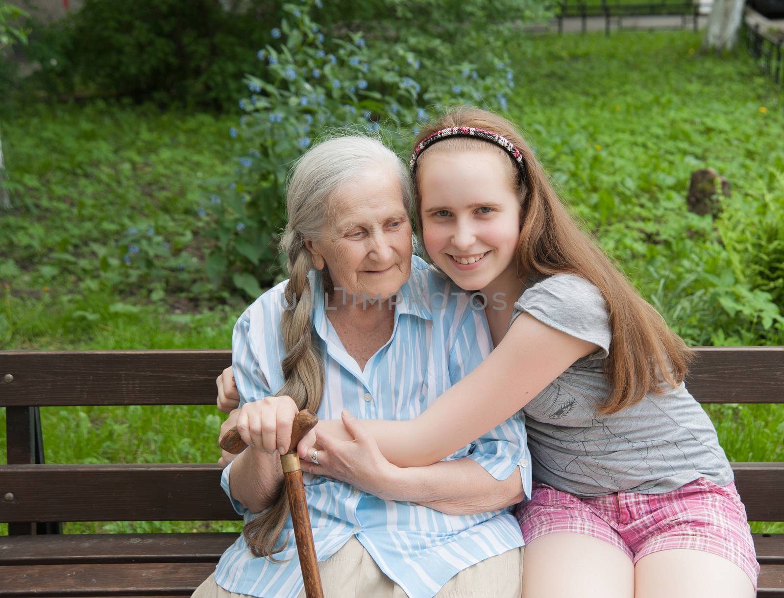 Granddaughter hugs grandmother sitting on a bench in the garden