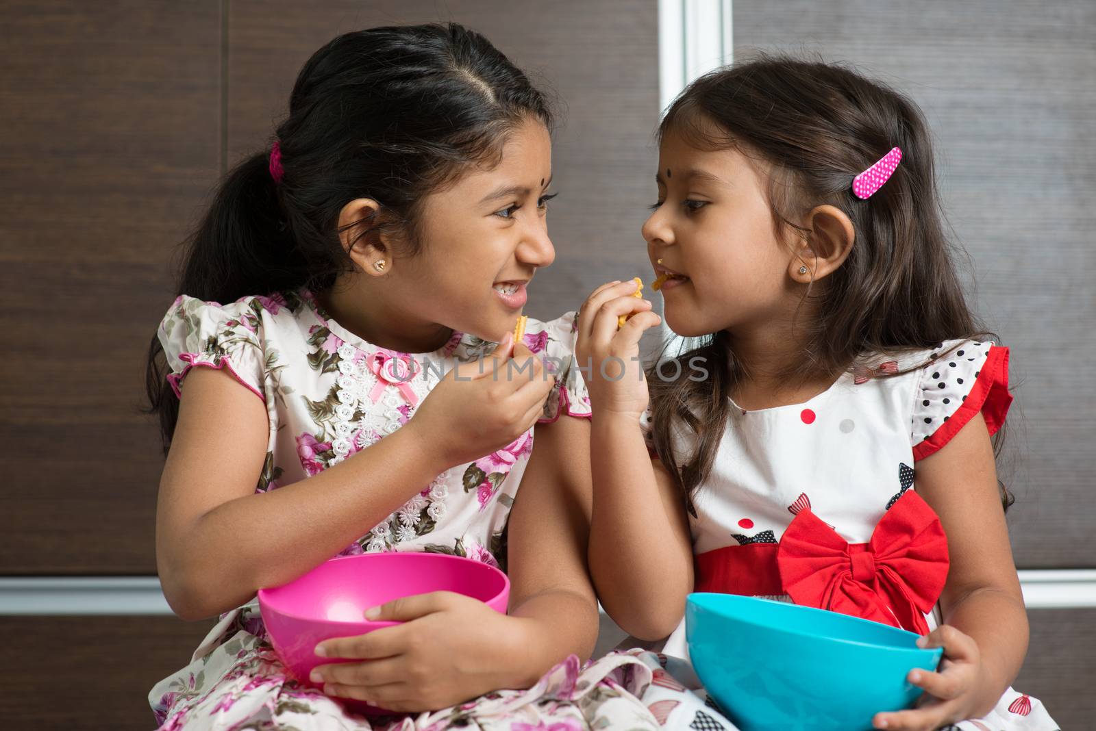 Two cute Indian girls eating murukku. Asian sibling or children living lifestyle at home.